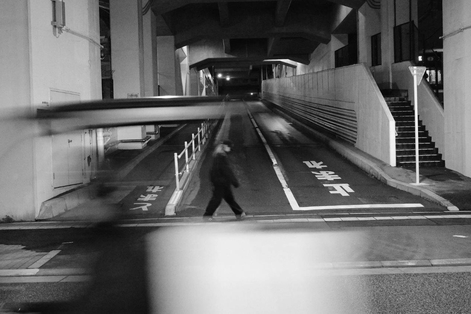 Photo en noir et blanc d'un piéton traversant la rue dans une ville nocturne