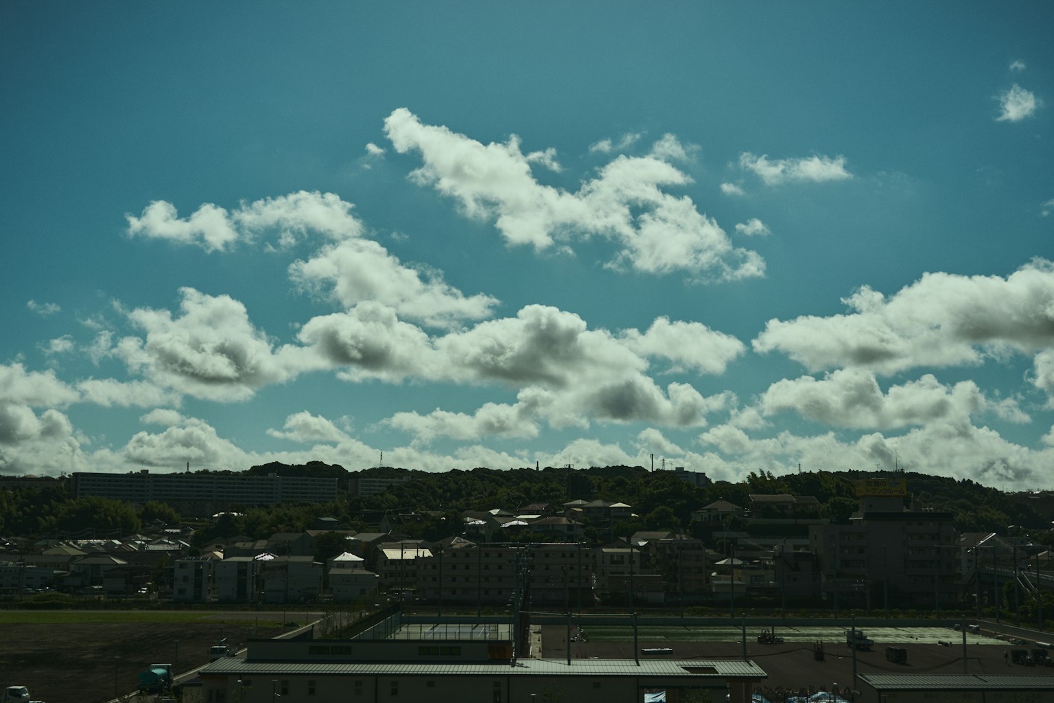 Landscape photo featuring blue sky and white clouds with houses and green hills