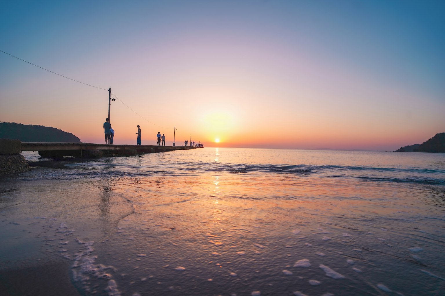 Schöner Sonnenuntergang über dem Ozean mit Menschen auf einem Pier und sanften Wellen