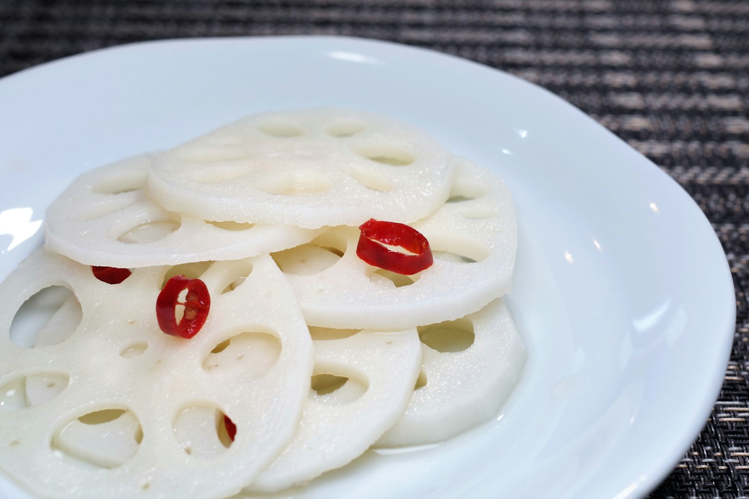 Scheiben von weißer Lotuswurzel garniert mit roten Chilischoten