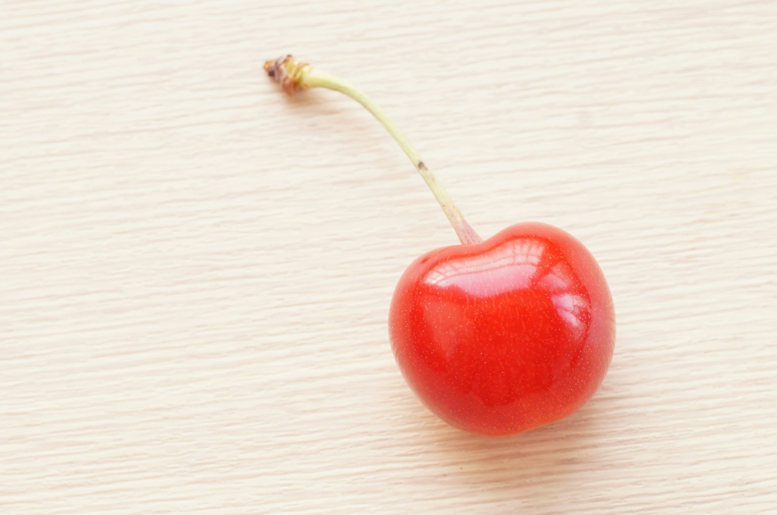 Một quả cherry đỏ tươi nằm trên bàn gỗ đơn giản