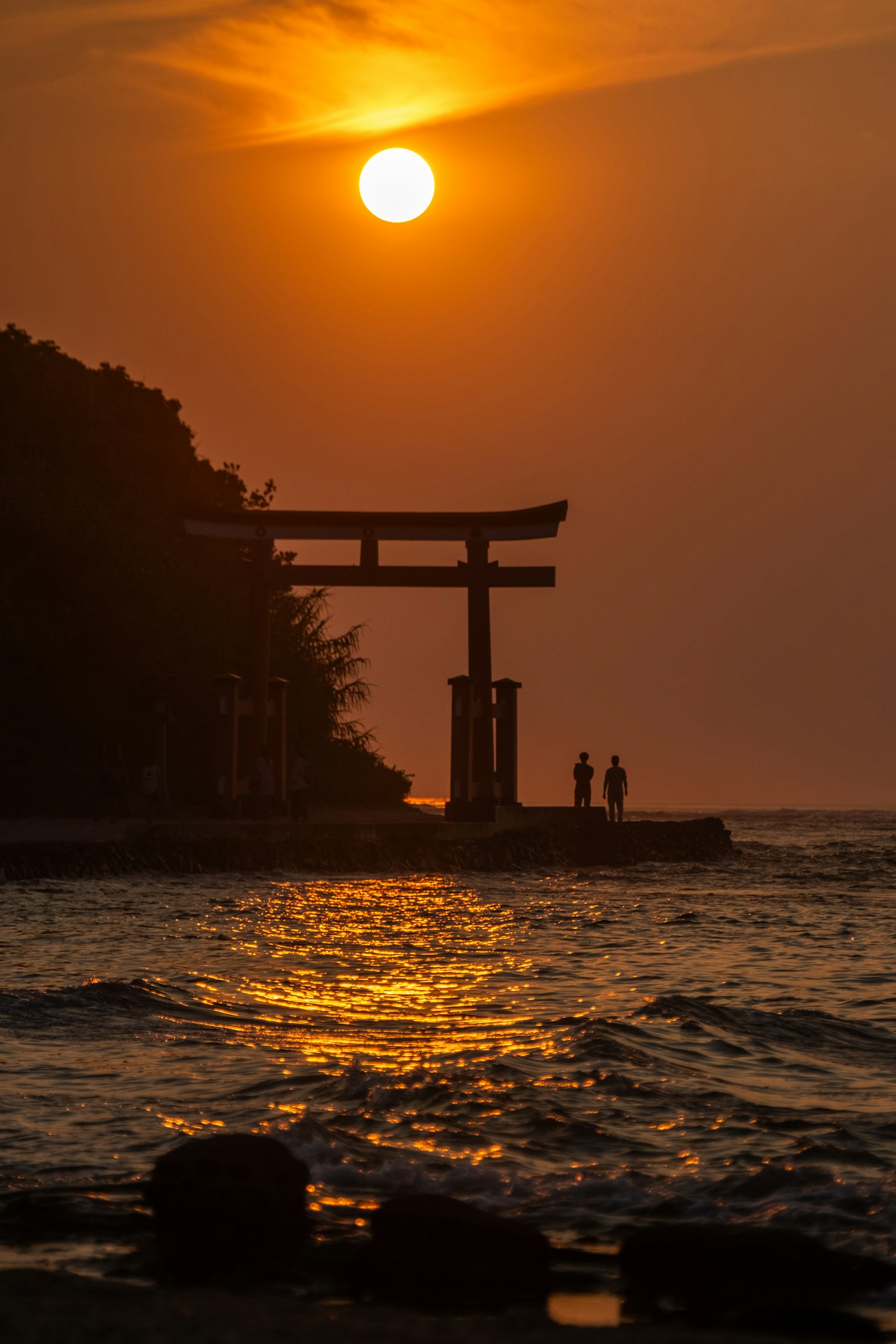 Silueta de un torii contra el atardecer junto al mar