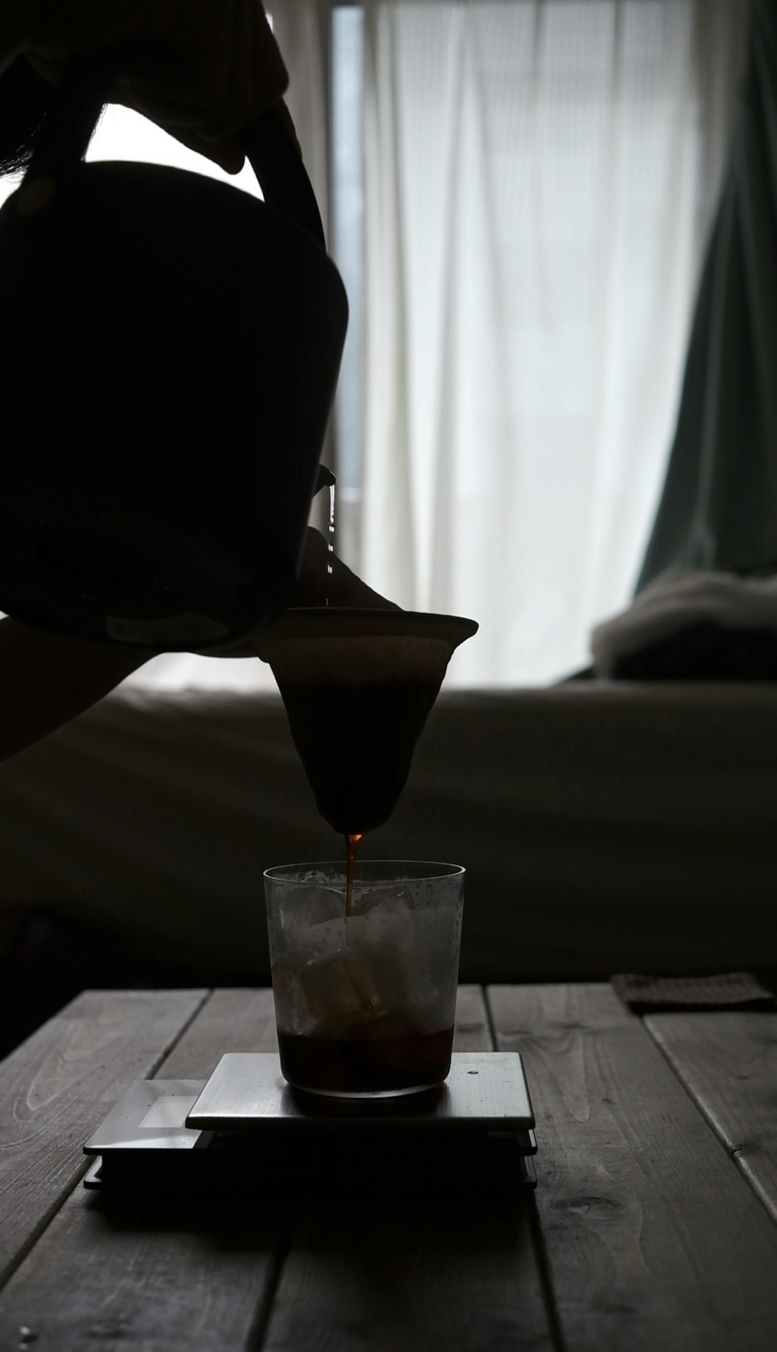 Silhouette des Kaffeegießens in ein Glas mit natürlichem Licht, das durch ein Fenster strömt