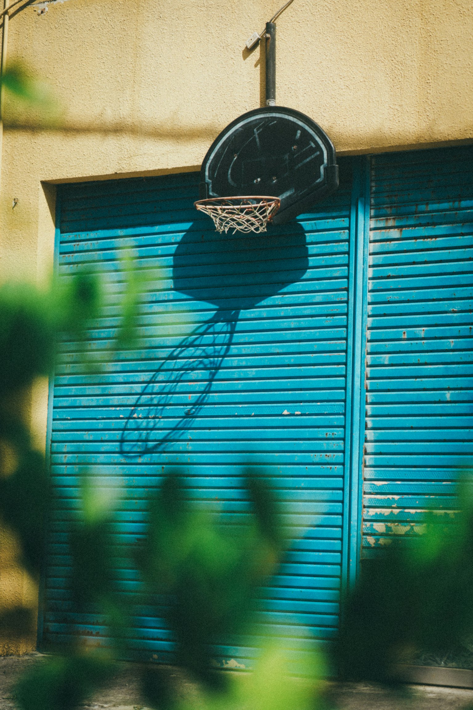 Aro de baloncesto montado en una pared con sombra proyectada sobre una persiana azul