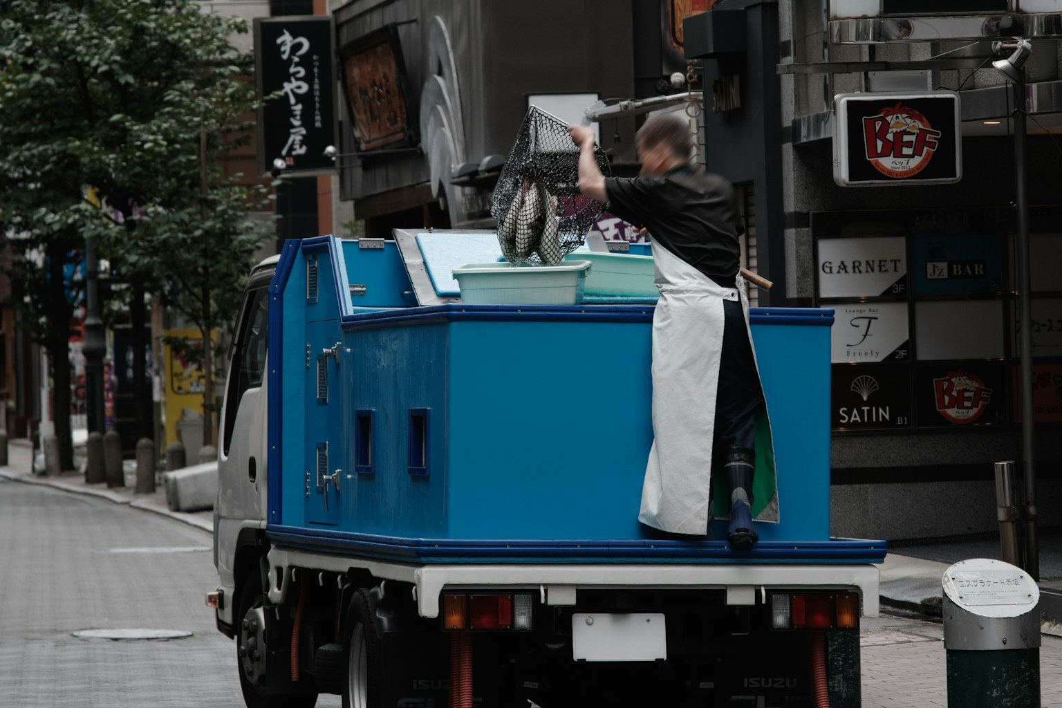 Man working on a blue truck in a city street