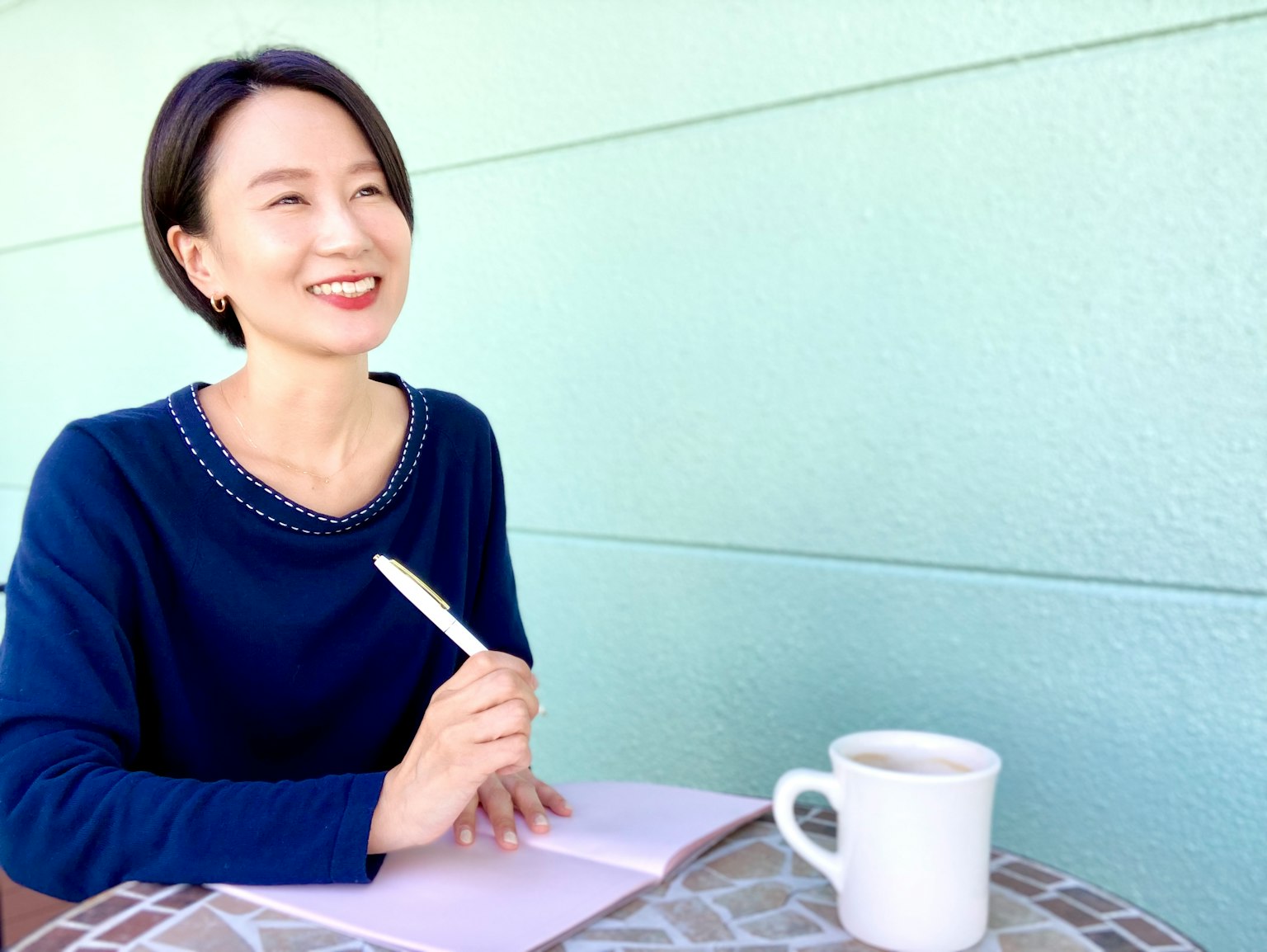 Una mujer sonriente con un suéter azul escribiendo en un cuaderno
