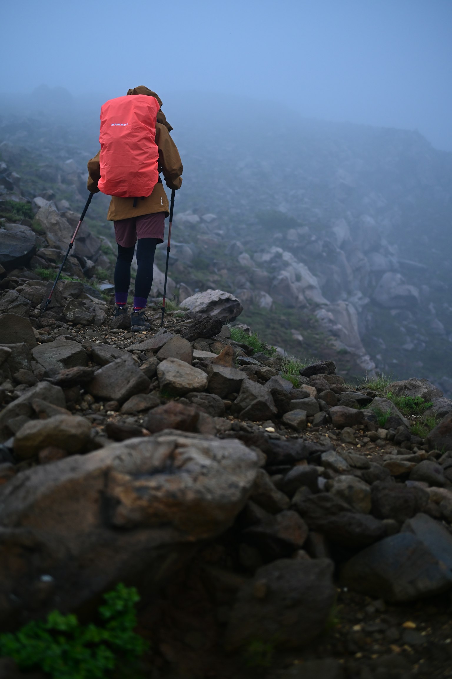 Wanderer, der durch den Nebel geht und einen großen orangefarbenen Rucksack trägt und über felsiges Gelände navigiert
