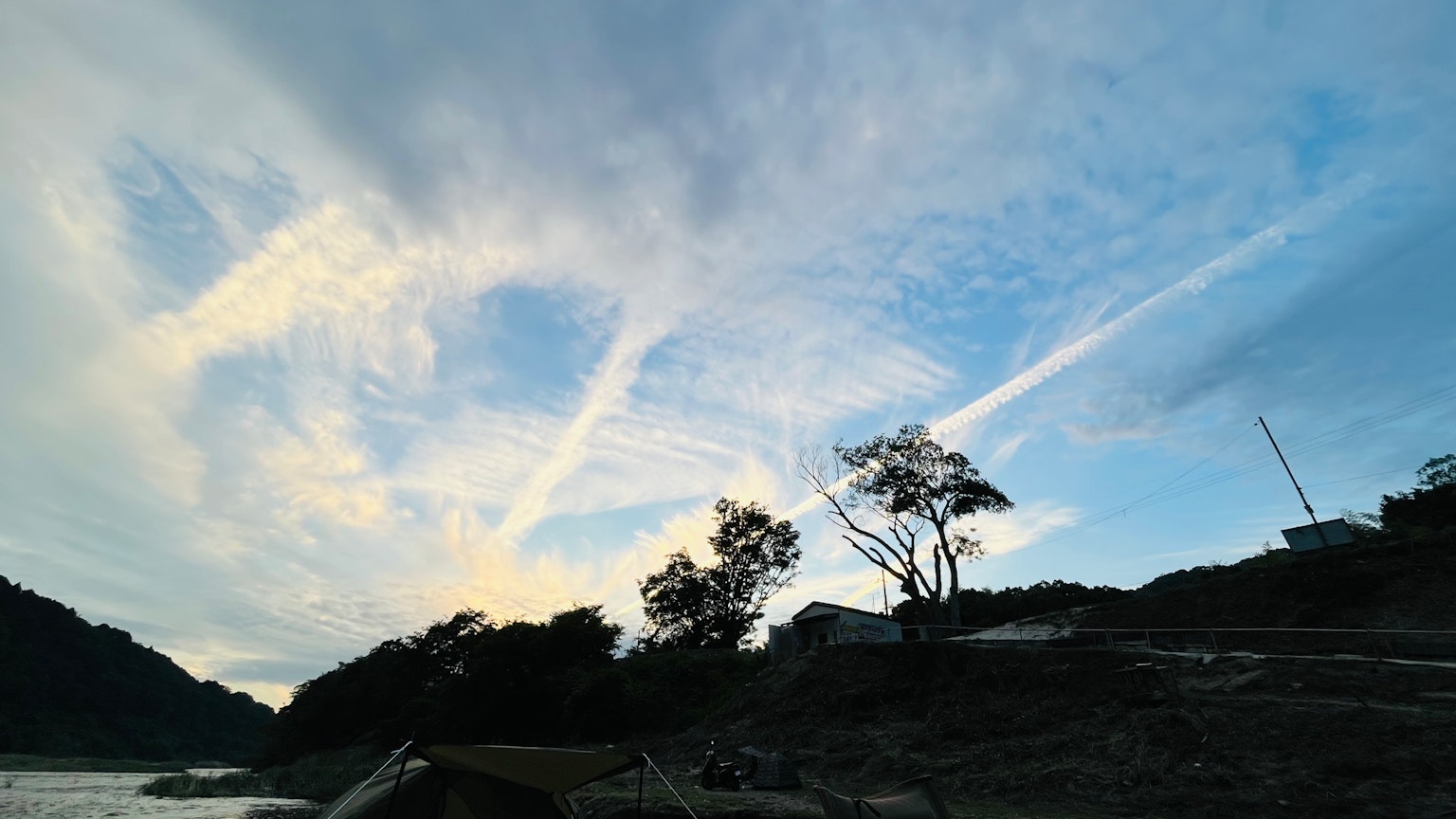 Landschaft mit blauem Himmel und Wolken mit silhouettierten Bäumen