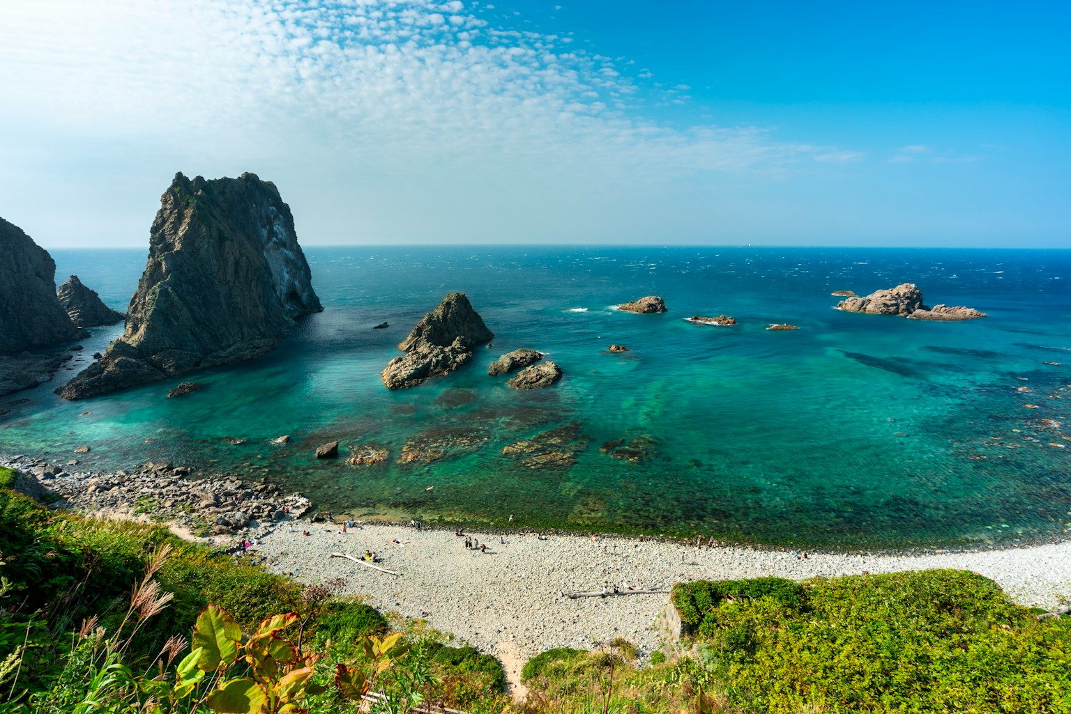 Vista panoramica di un mare calmo e formazioni rocciose con vegetazione verde lungo la spiaggia
