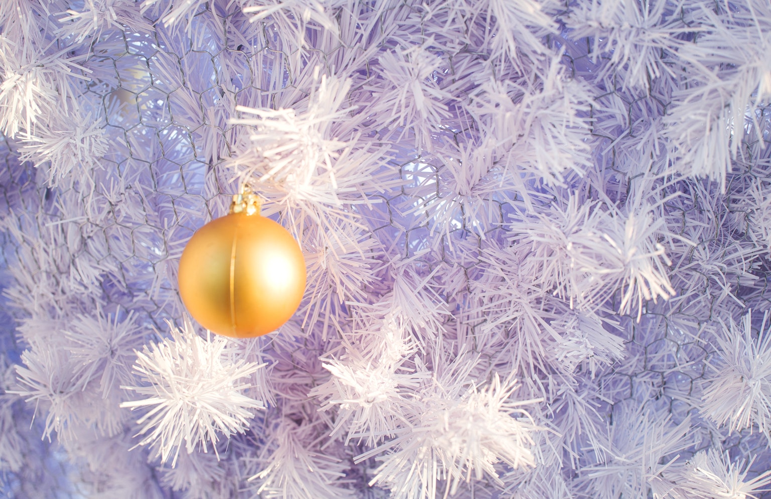A white Christmas tree with a golden ornament hanging