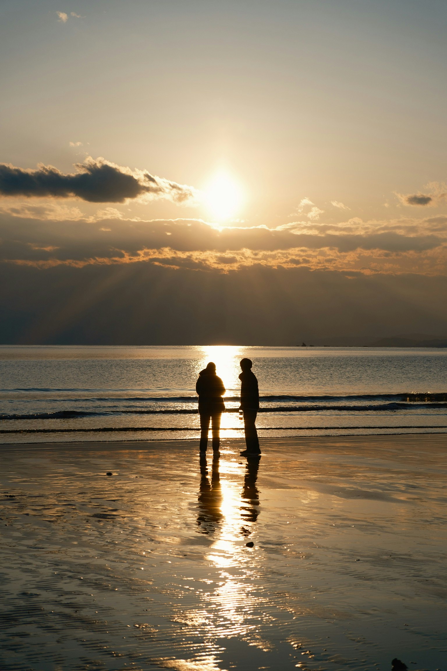 夕焼けの海辺で寄り添うシルエットの二人