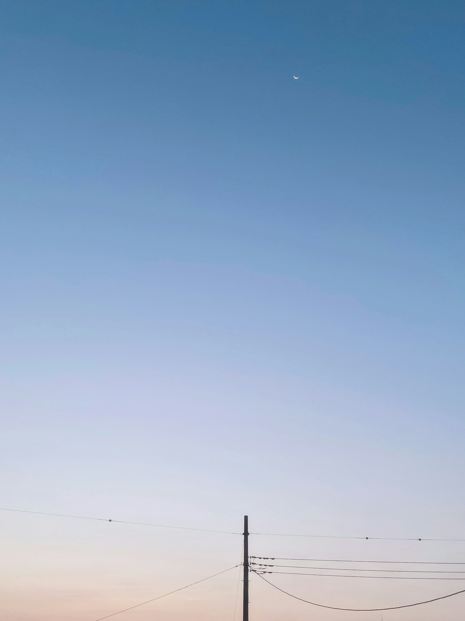 A serene sky with a crescent moon and a power pole