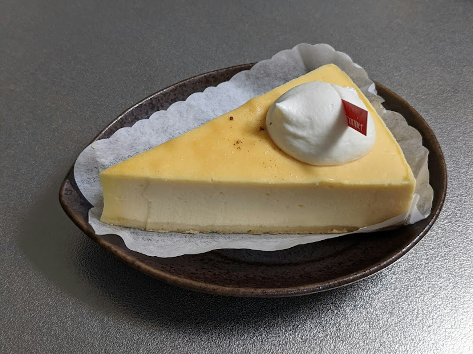 Stück gelber Käsekuchen mit Schlagsahne und rohem Topping auf einem braunen Teller