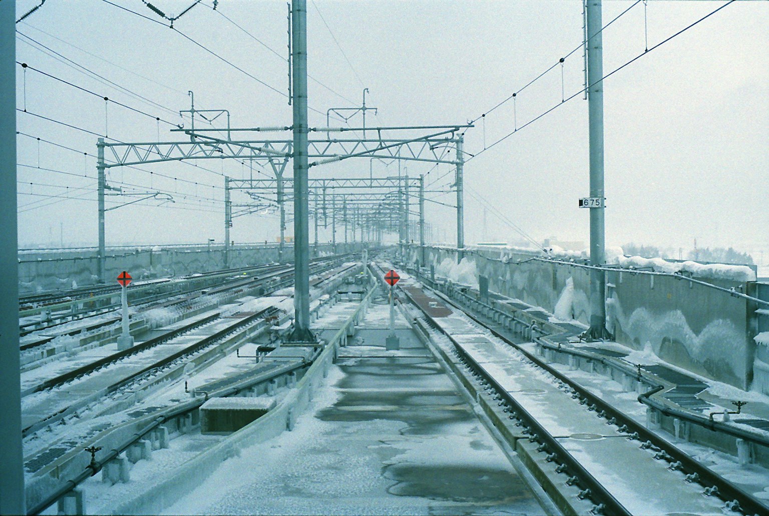 รางรถไฟที่มีหิมะปกคลุมและสายไฟเหนือศีรษะในภูมิทัศน์ฤดูหนาว