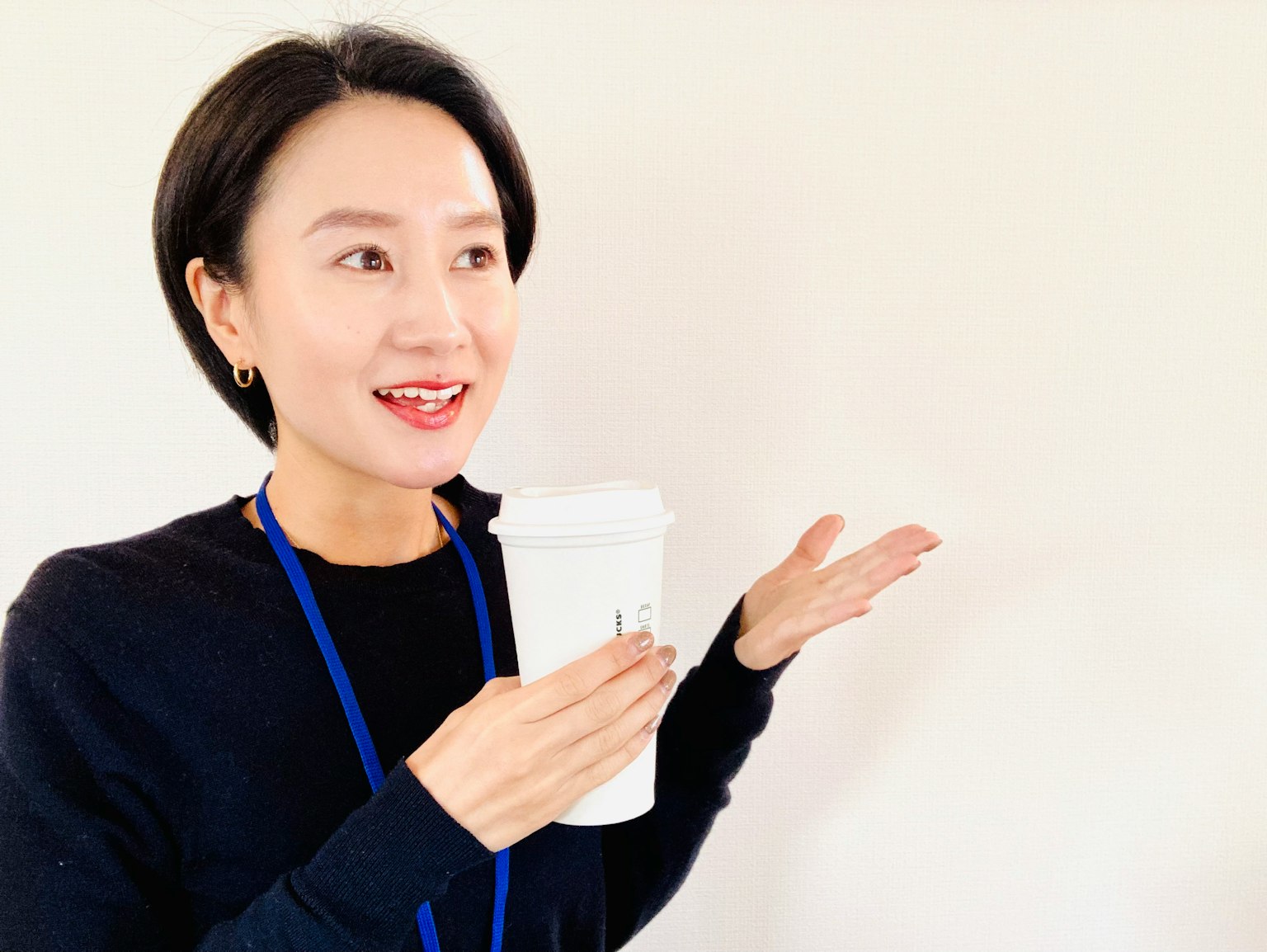 A woman speaking while holding a coffee cup in front of a white background