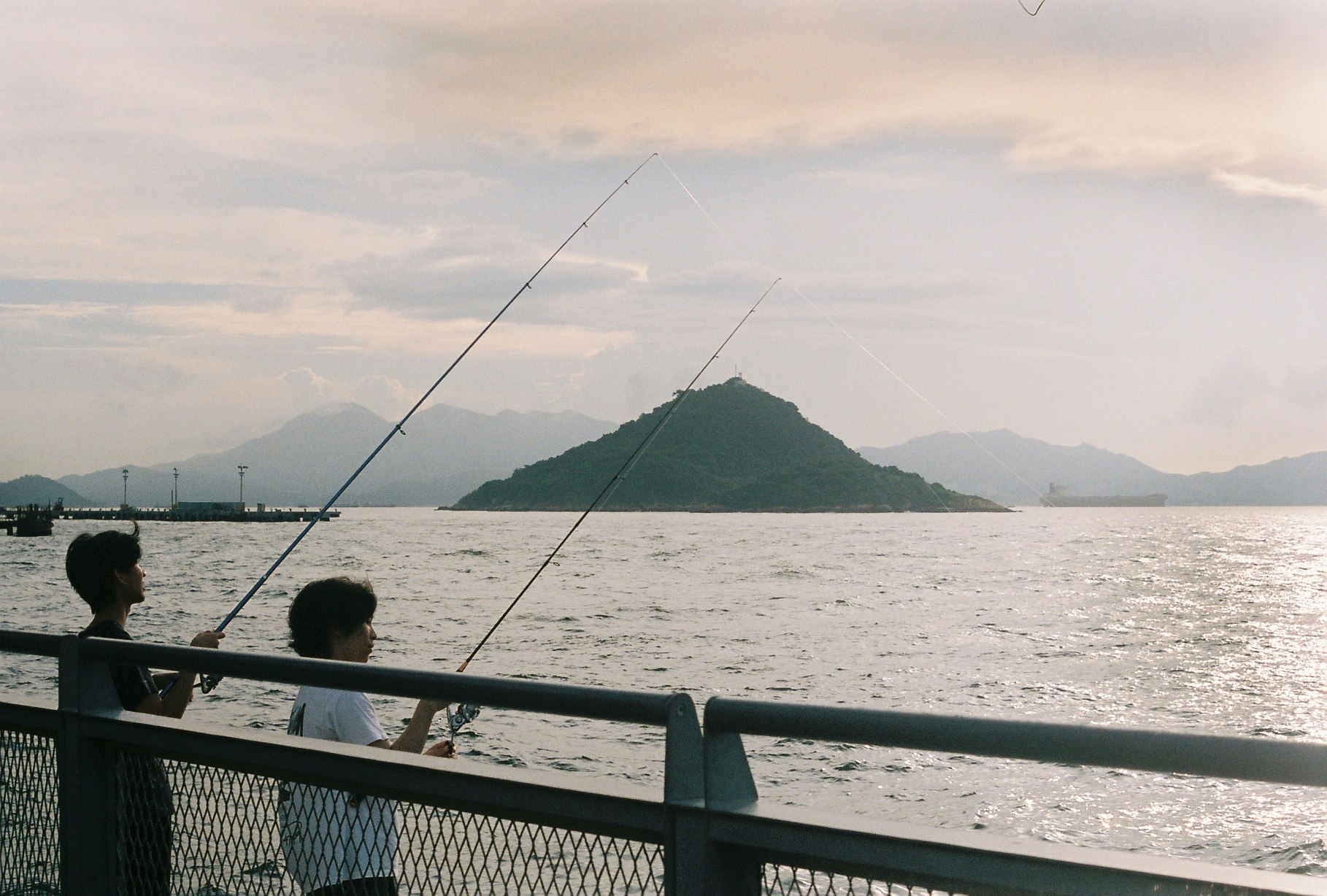 海上の桟橋で釣りをする人と島の風景