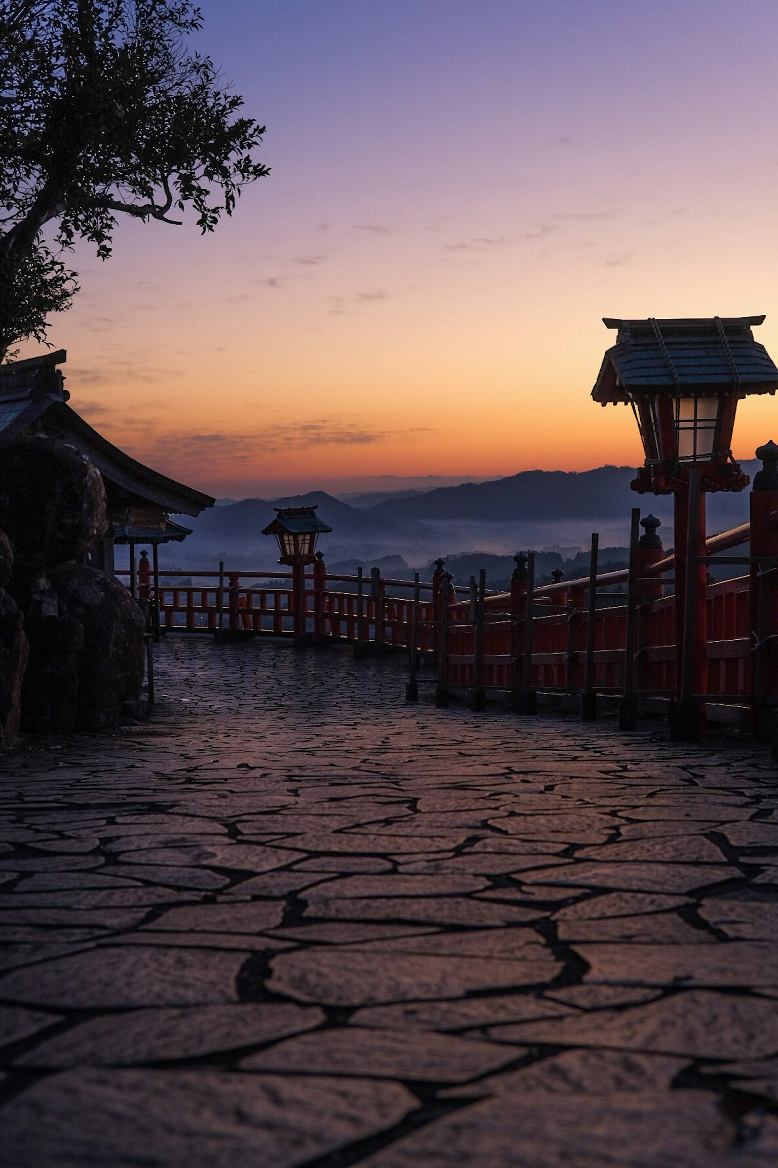 夕焼けの中の石畳の道と赤い手すりの橋が見える風景
