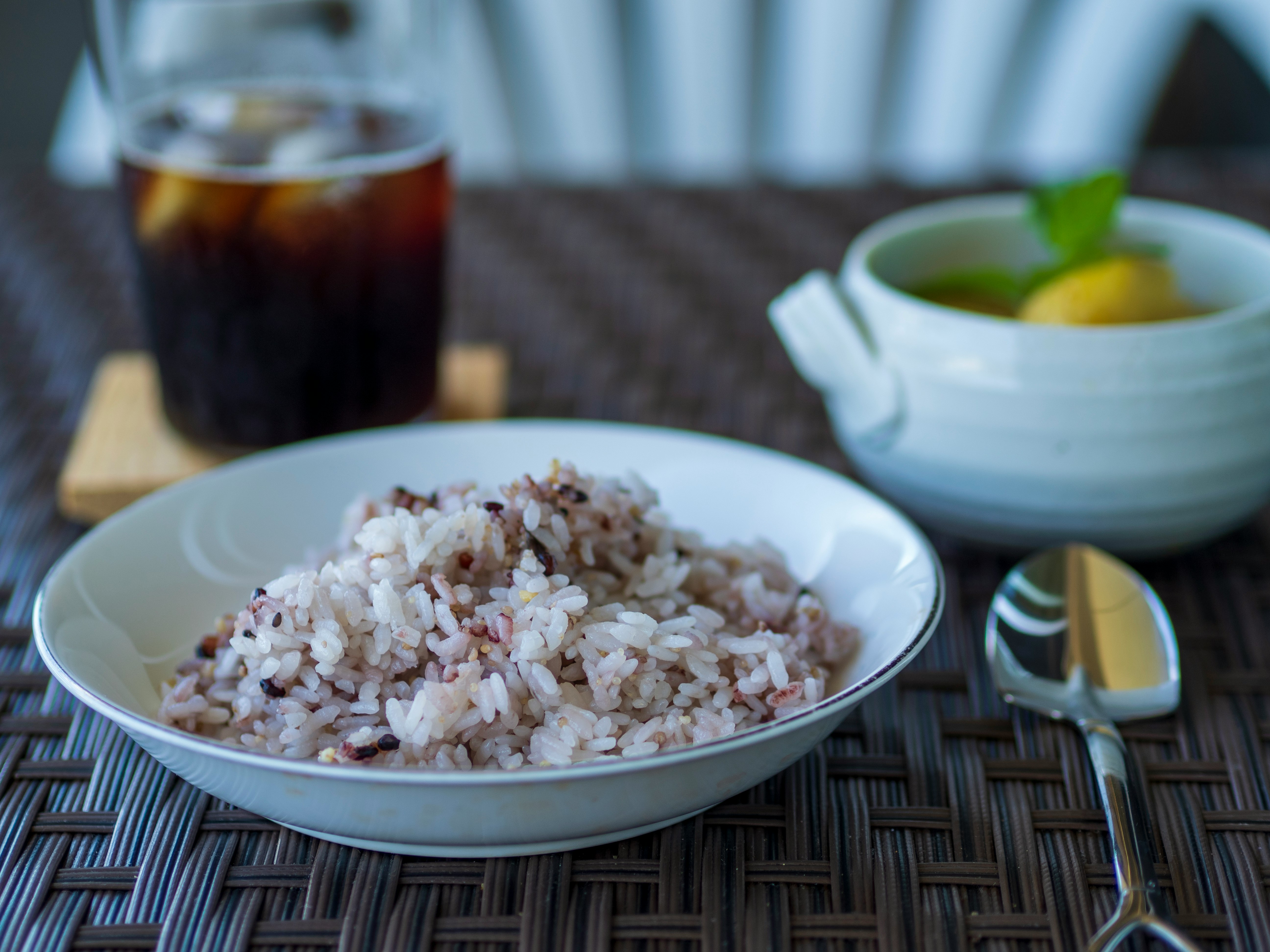 bowl of rice with lemon and a glass of iced drink on a woven table