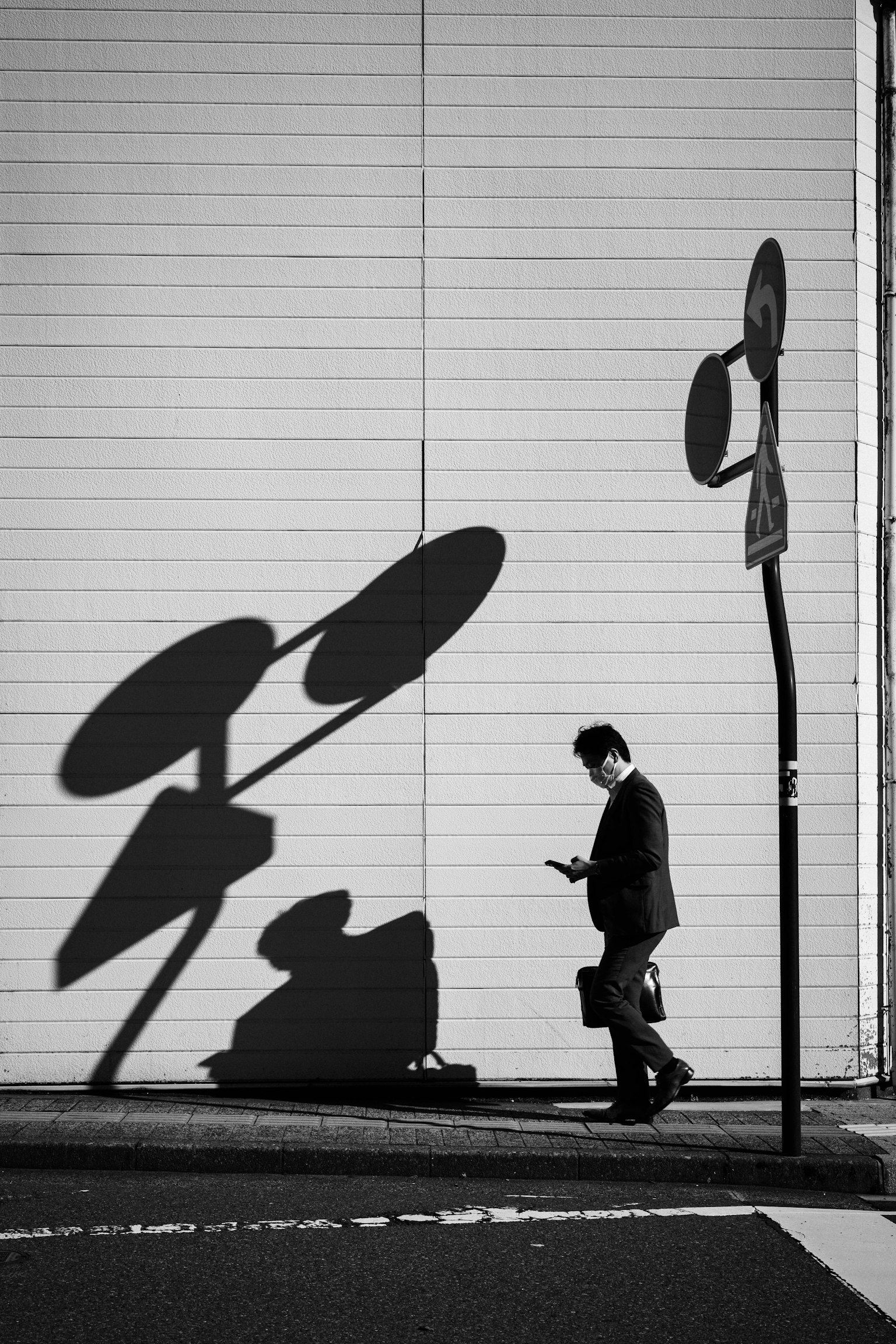 Geschäftsmann, der an einer Wand vorbeigeht und auf sein Smartphone-Schatten schaut