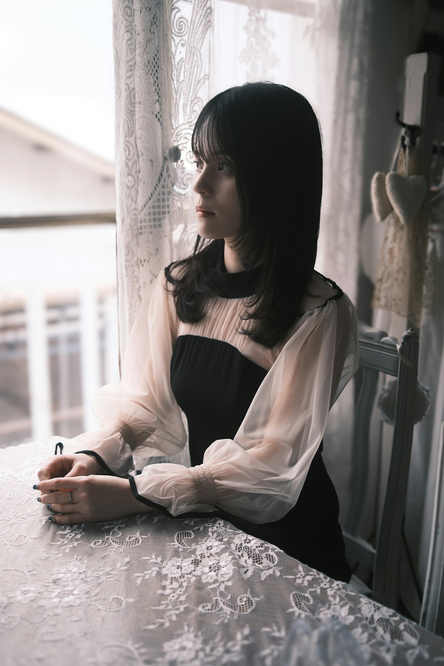 窓辺に座る女性の横顔 黒いドレスと白いブラウスの組み合わせ 繊細なレースのカーテンが背景にある