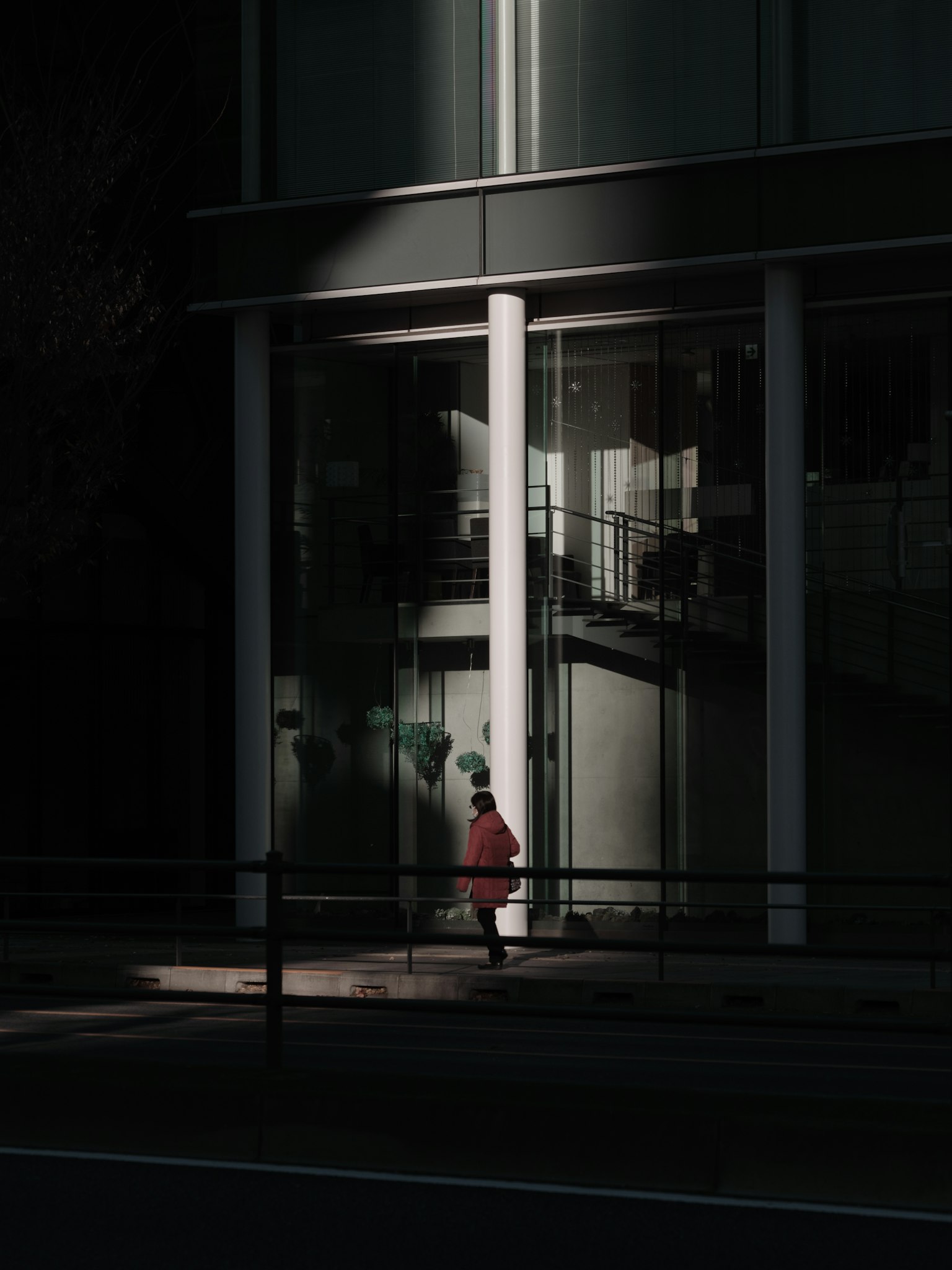 Una persona in un abito rosso che cammina davanti a un edificio con ombre scure