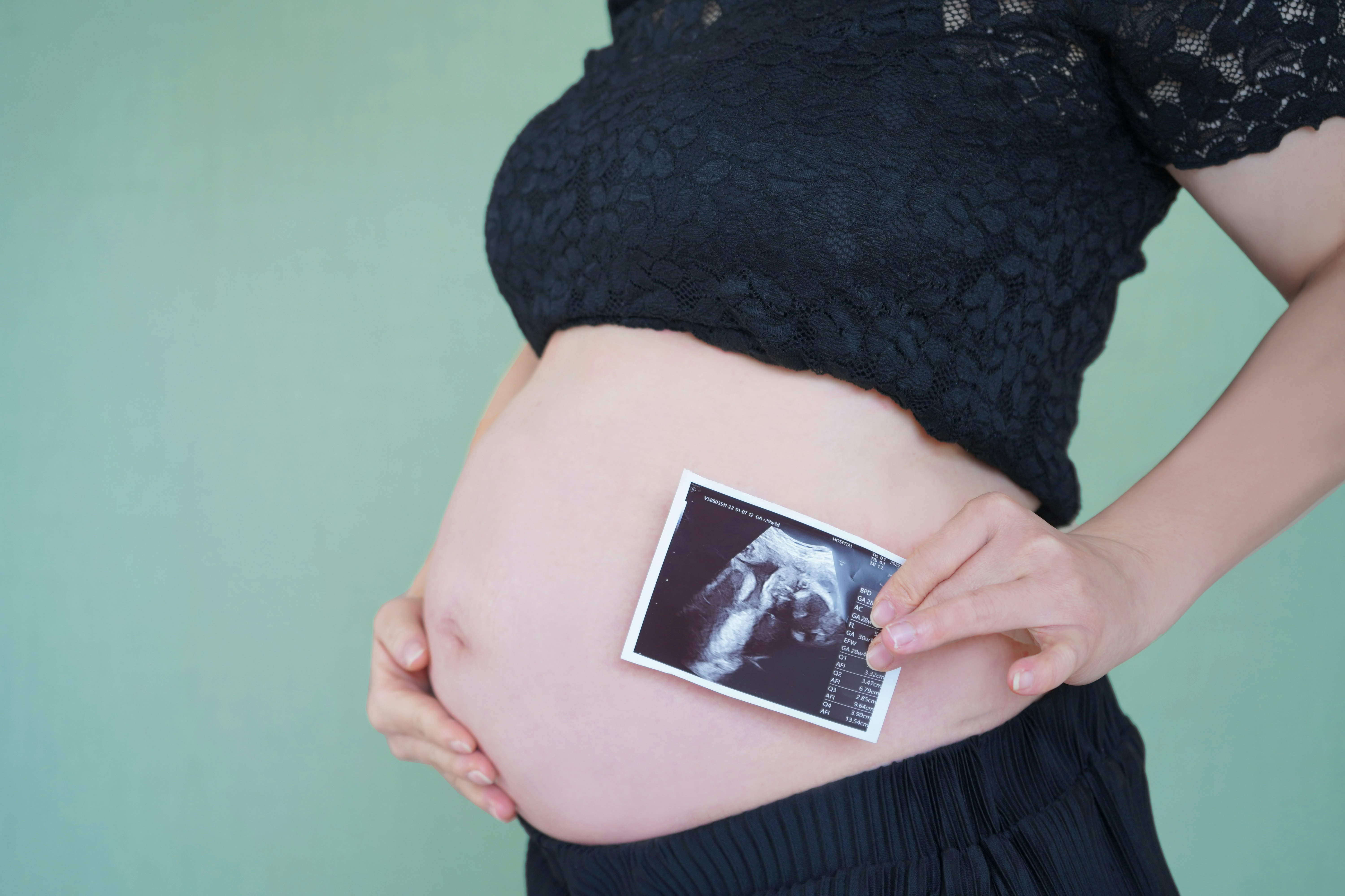 黒いレースの服を着た妊婦がエコー写真を抱える