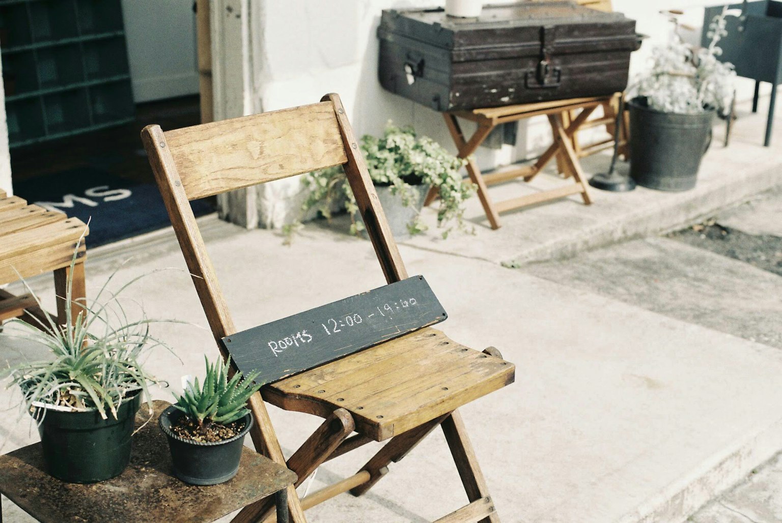 Wooden chair with a sign and small plant pots at a cafe entrance