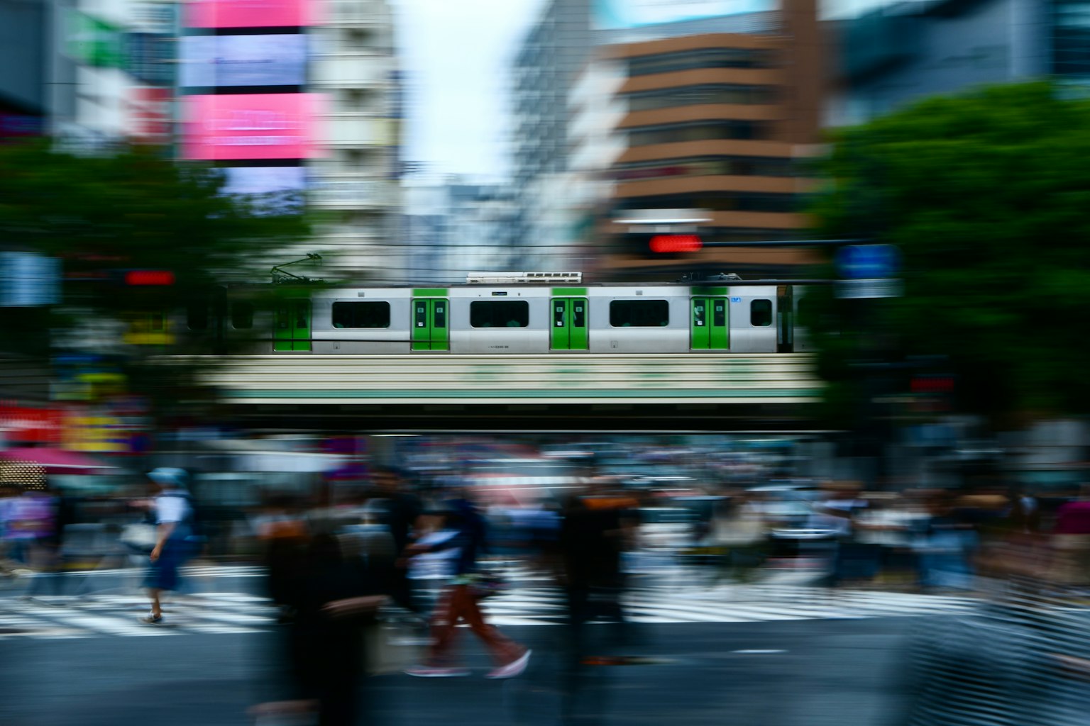 模糊的城市景象中，綠色列車經過擁擠的交叉口