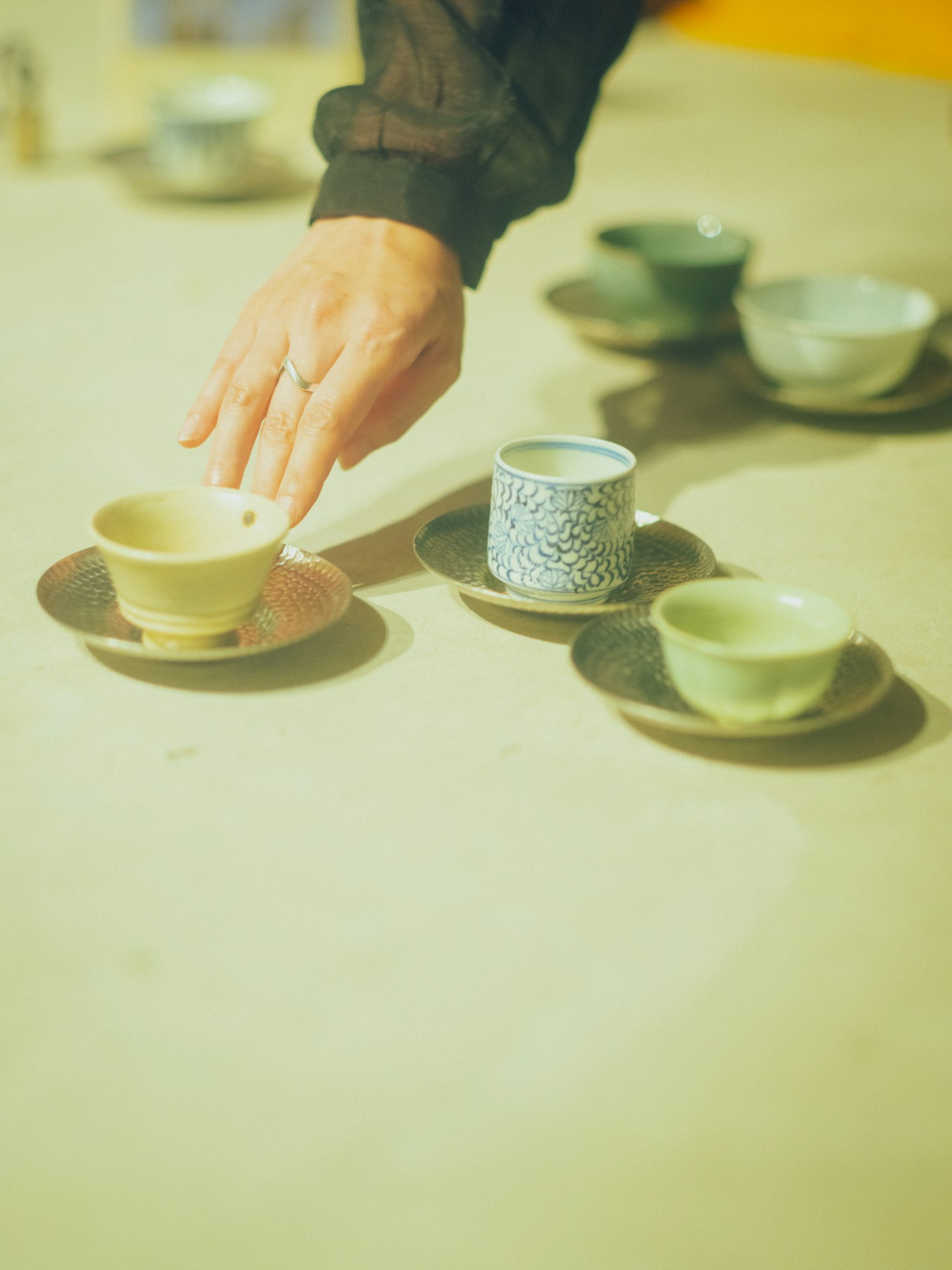 一只手将茶碗放在桌子上，背景中有多彩的茶碗
