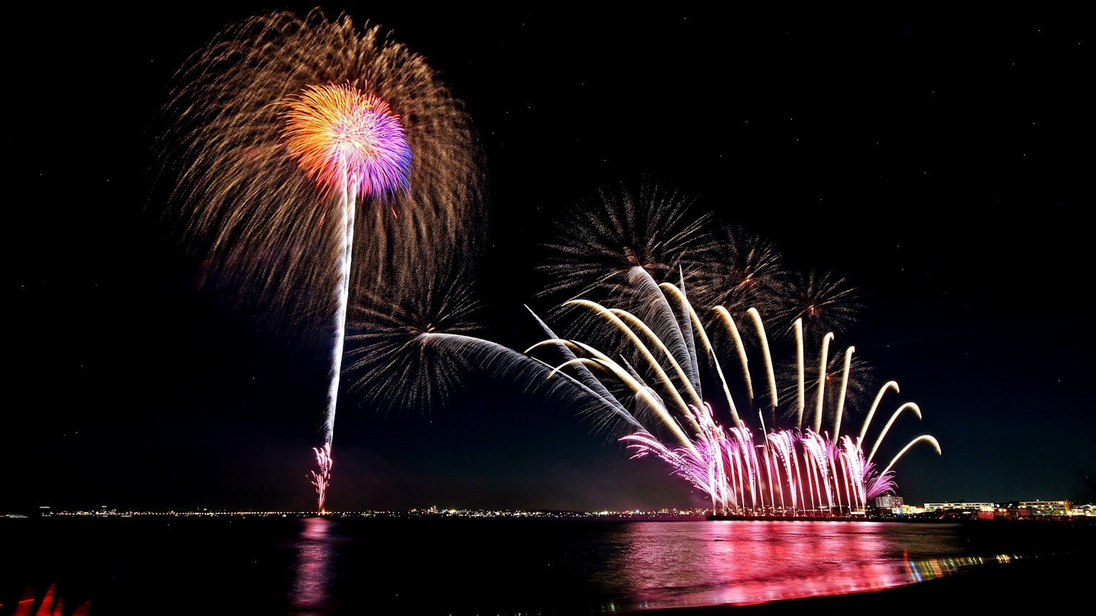 Spettacolo di fuochi d'artificio colorati nel cielo notturno riflessi sull'acqua