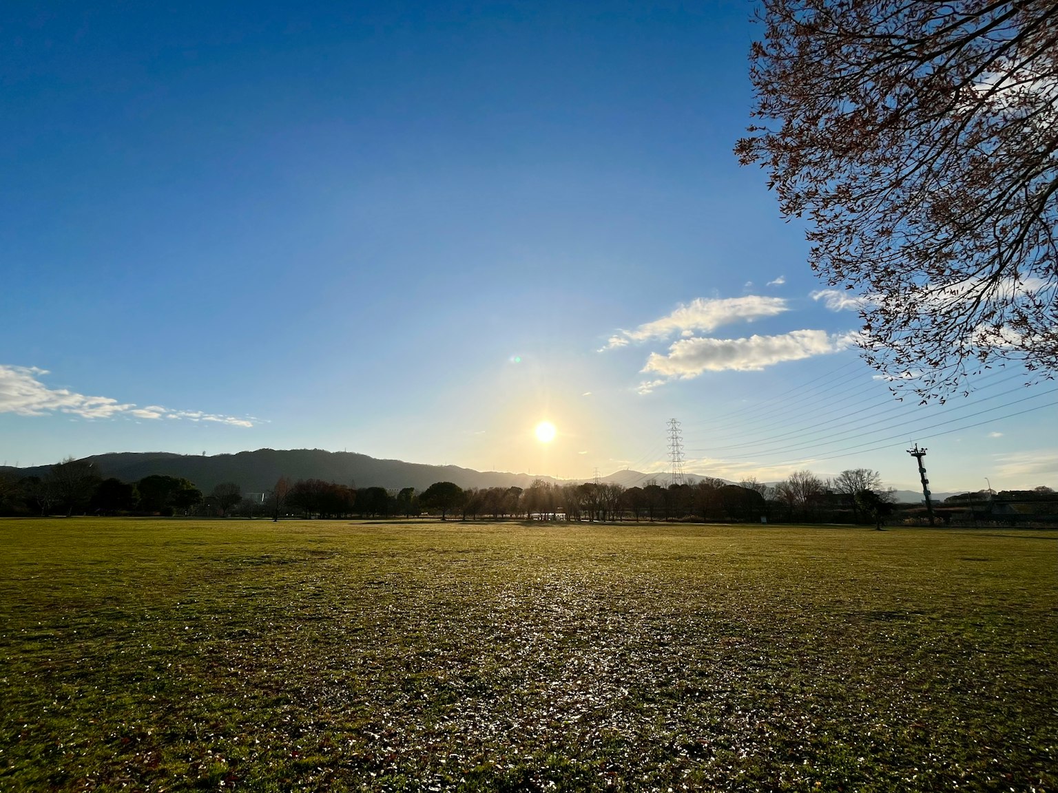 Paesaggio con sole che sorge sotto un cielo blu campo verde e silhouette di montagne