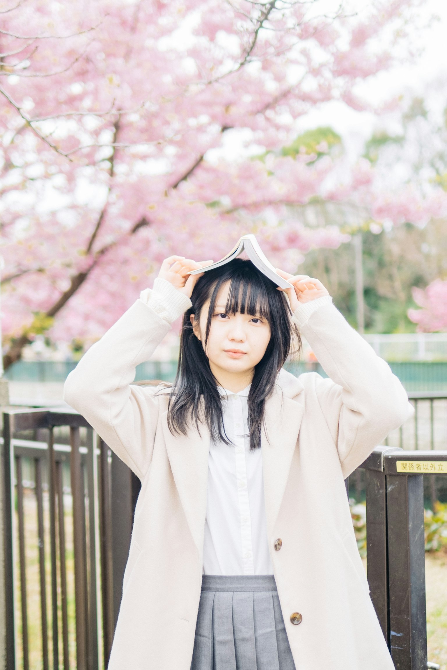 Woman in a coat holding a hat in front of cherry blossom trees