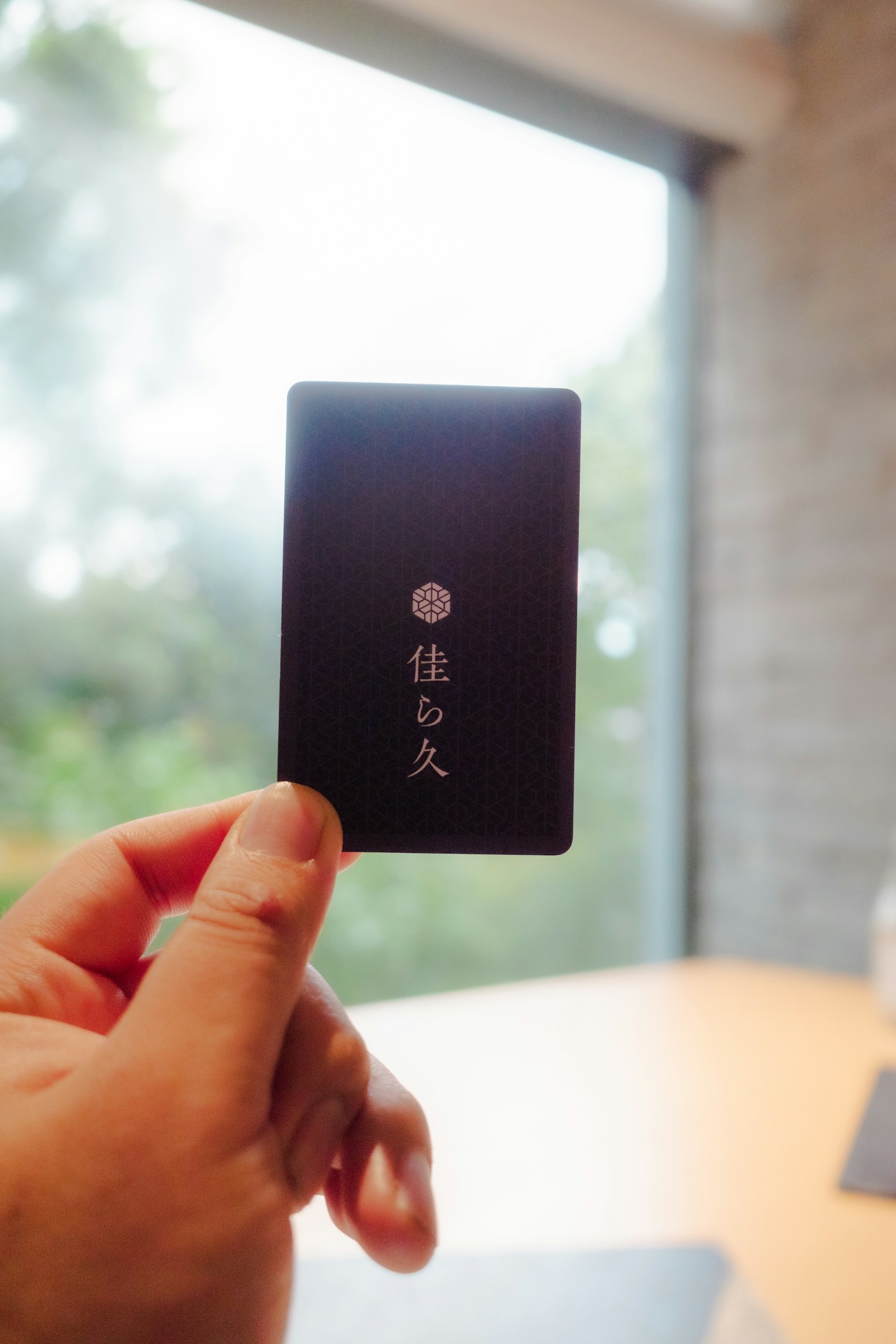 Cận cảnh bàn tay cầm thẻ đen có chữ Nhật và ánh sáng tự nhiên từ cửa sổ phía sau