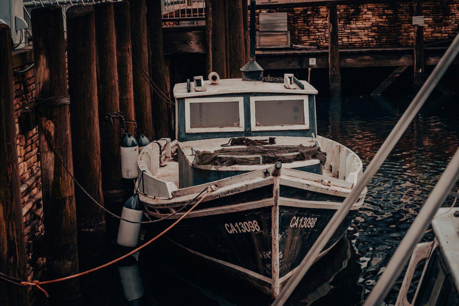 A small boat docked in a quiet harbor with wooden pilings