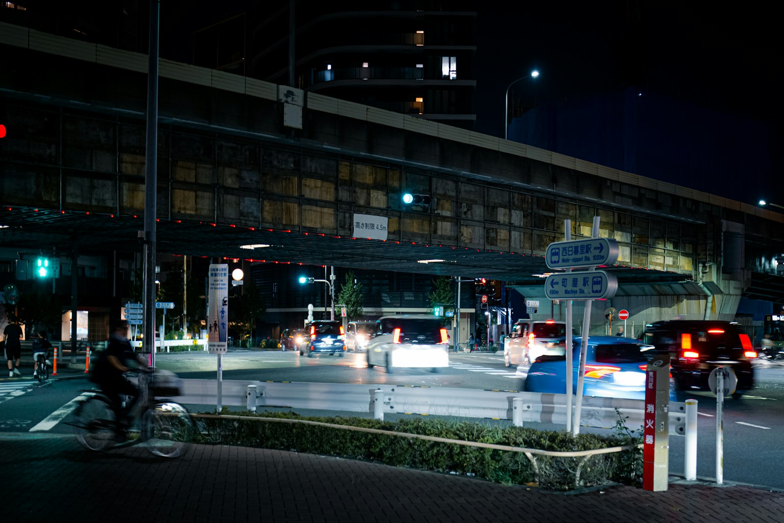 Paesaggio urbano notturno con un incrocio affollato biciclette e auto sotto una strada sopraelevata