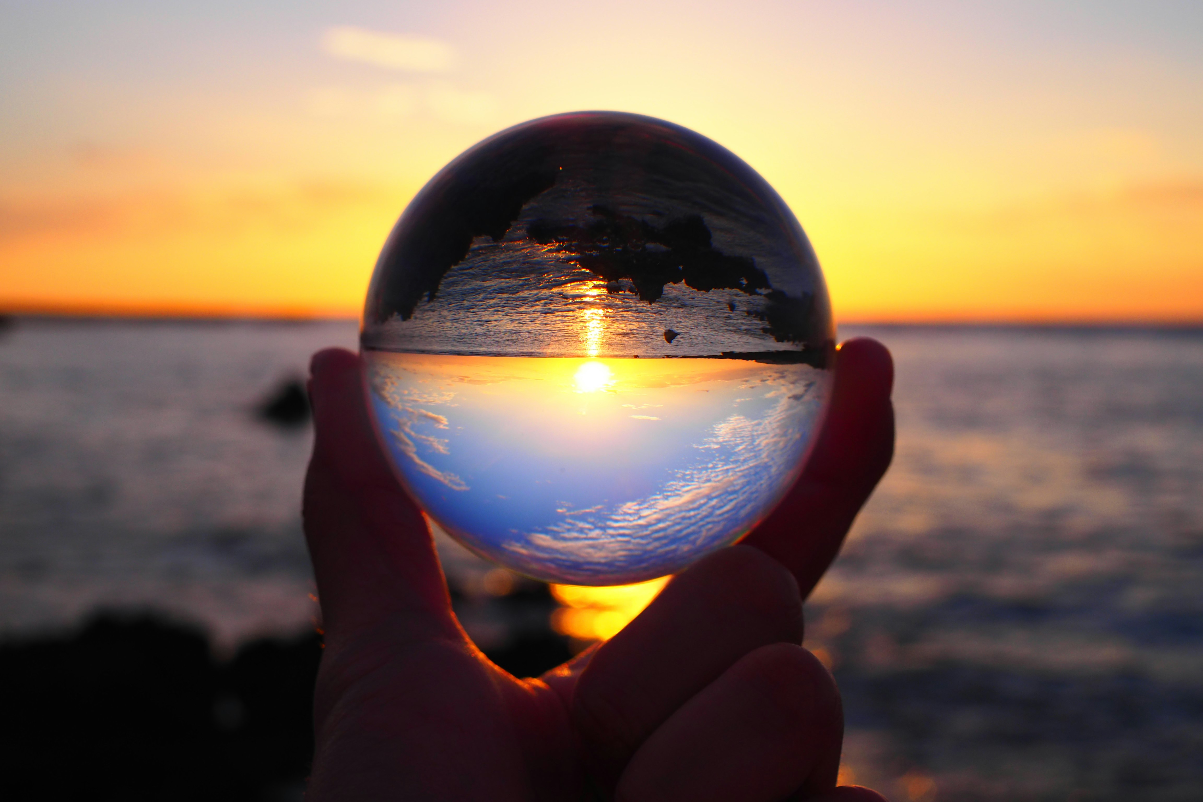 夕日に照らされた海を手のひらで映す逆さの球体
