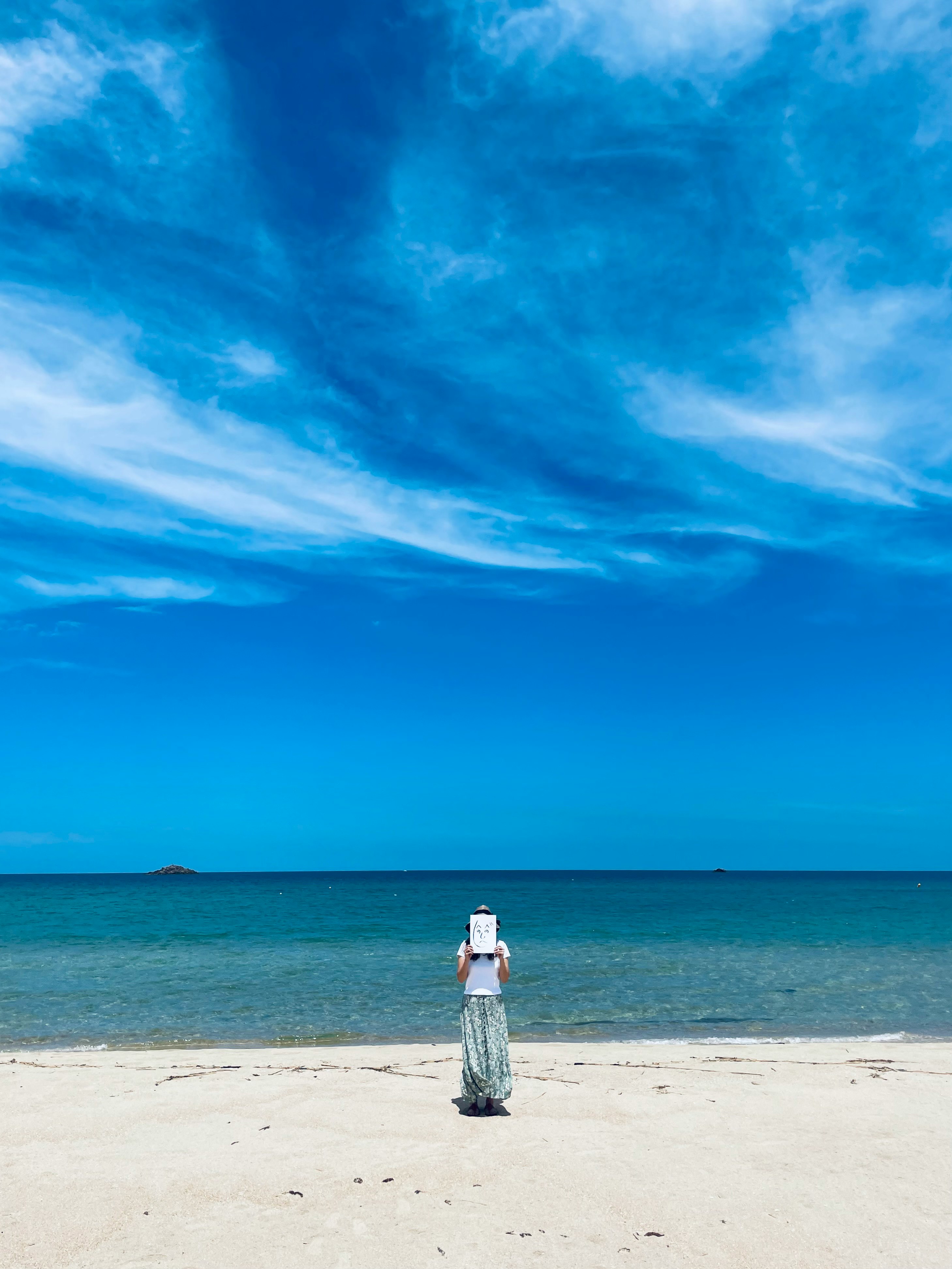 青い空と海を背景に砂浜を歩く女性