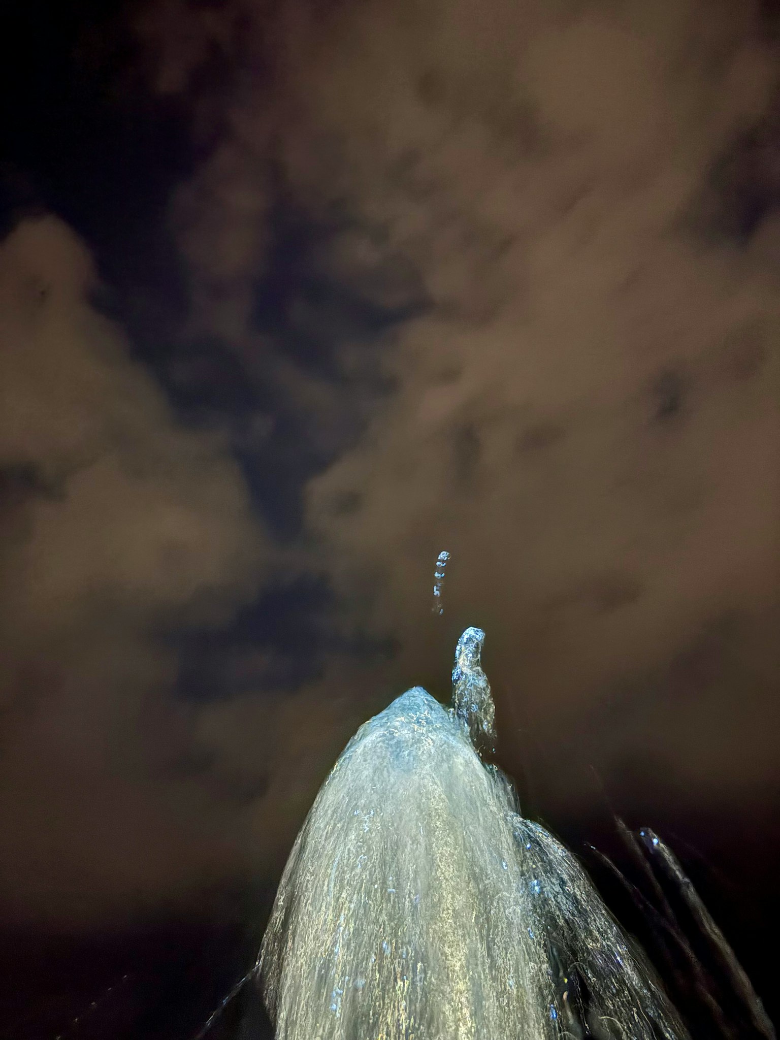 夜空に向かって噴き上がる水の噴水と雲