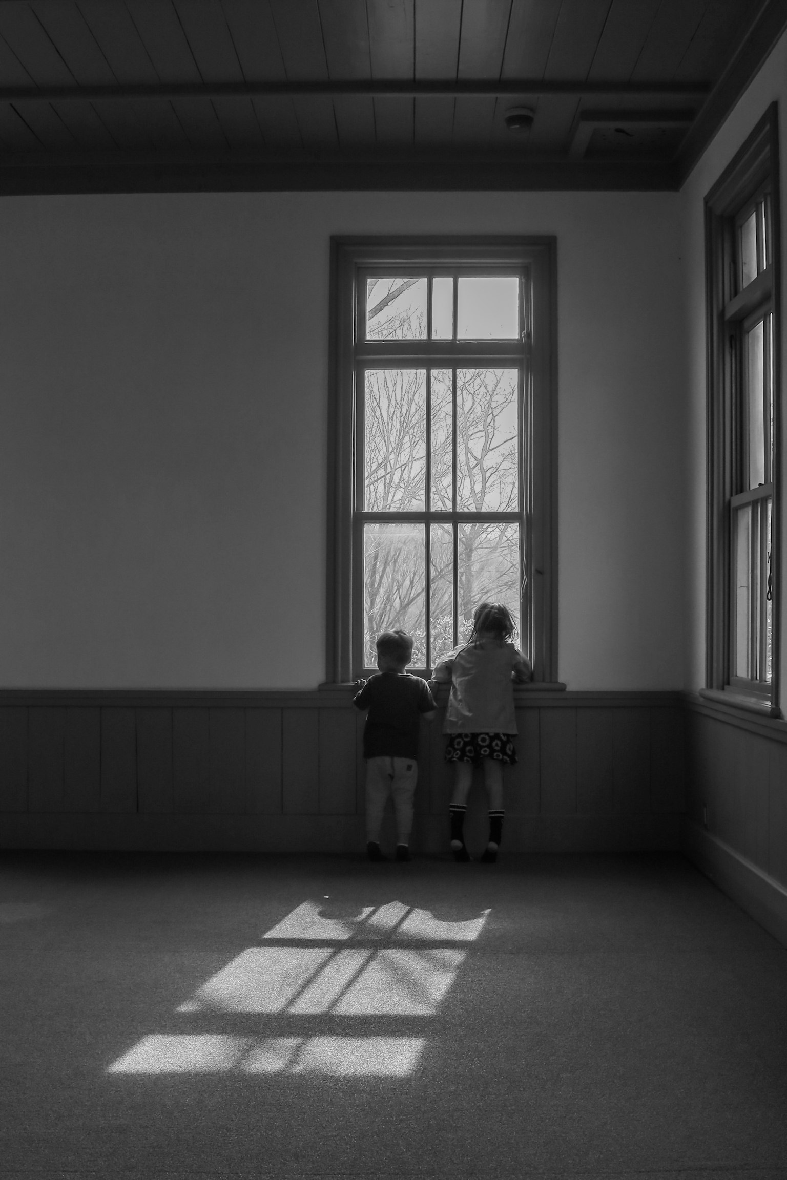 Dos niños mirando por la ventana en una habitación en blanco y negro