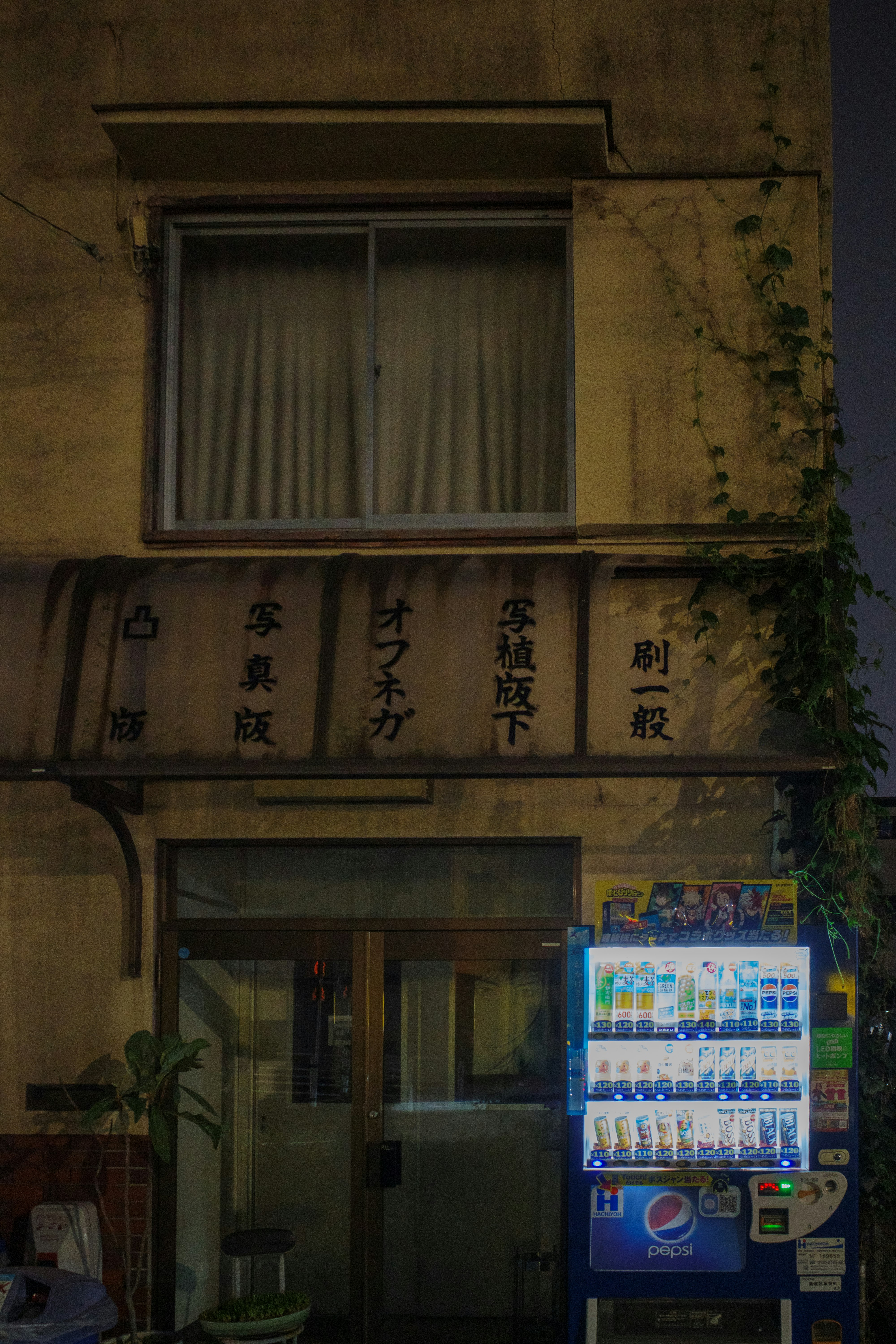 路地の古い建物の軒先に並ぶ看板と自動販売機