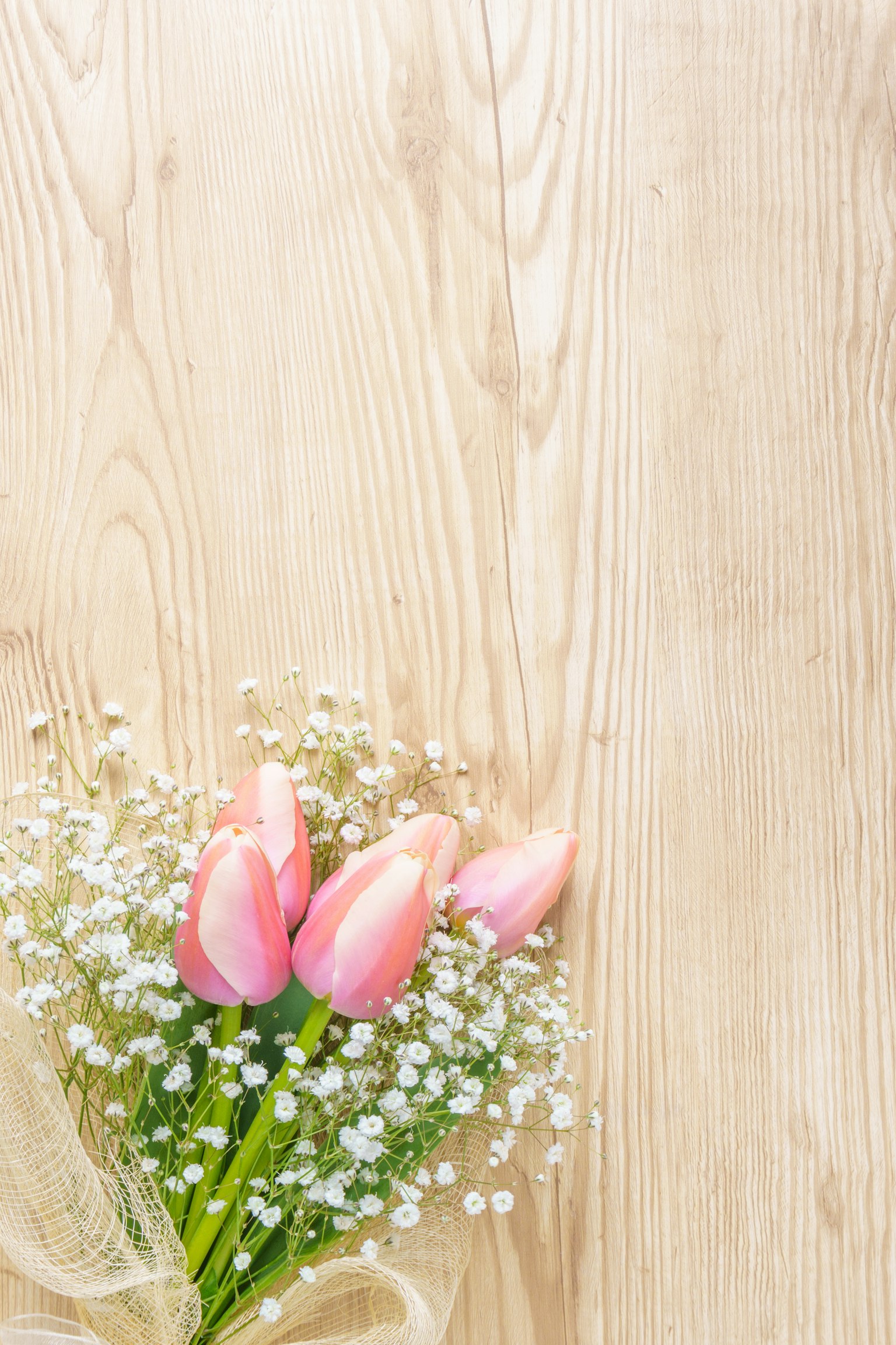 Sekuntum tulip merah muda dengan napas bayi di atas meja kayu