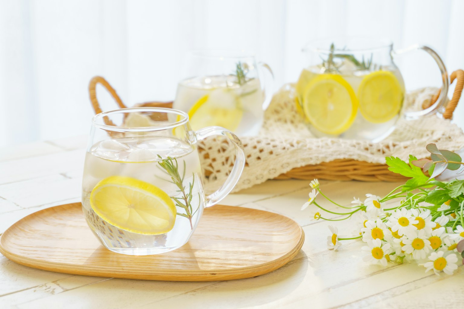 Klare Gläser mit Zitronen- und Minzwasser auf einem Holztablett mit floraler Dekoration
