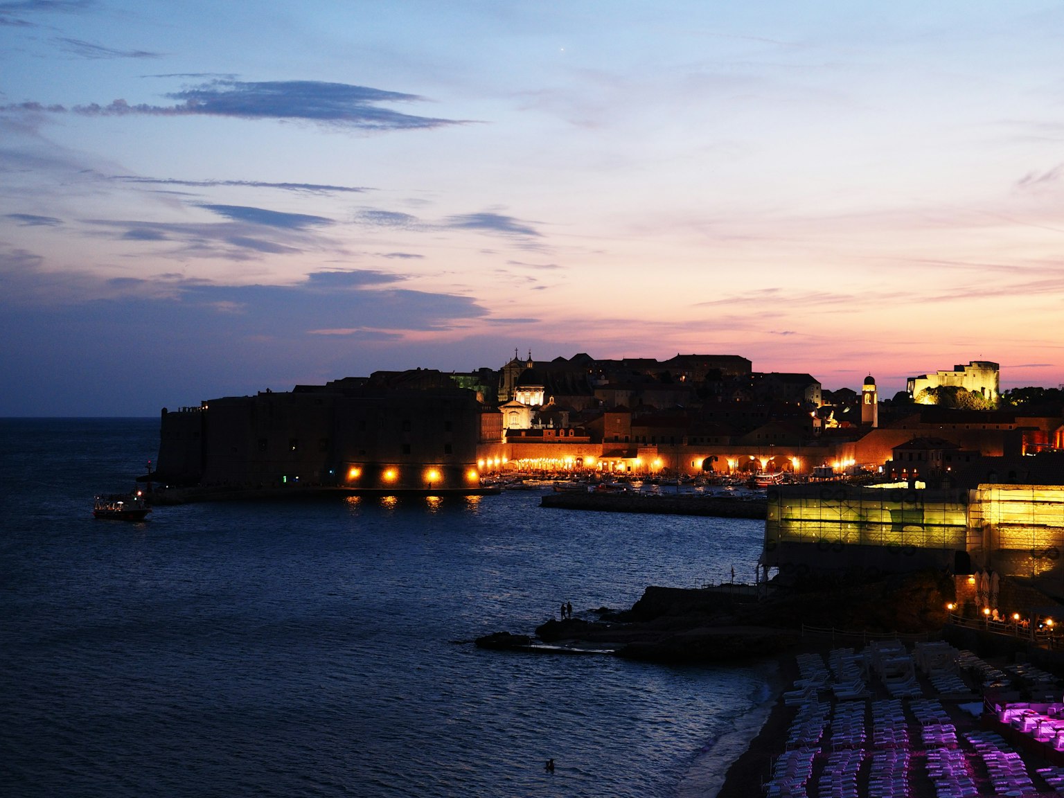 Paesaggio costiero al tramonto con edifici illuminati e mare tranquillo