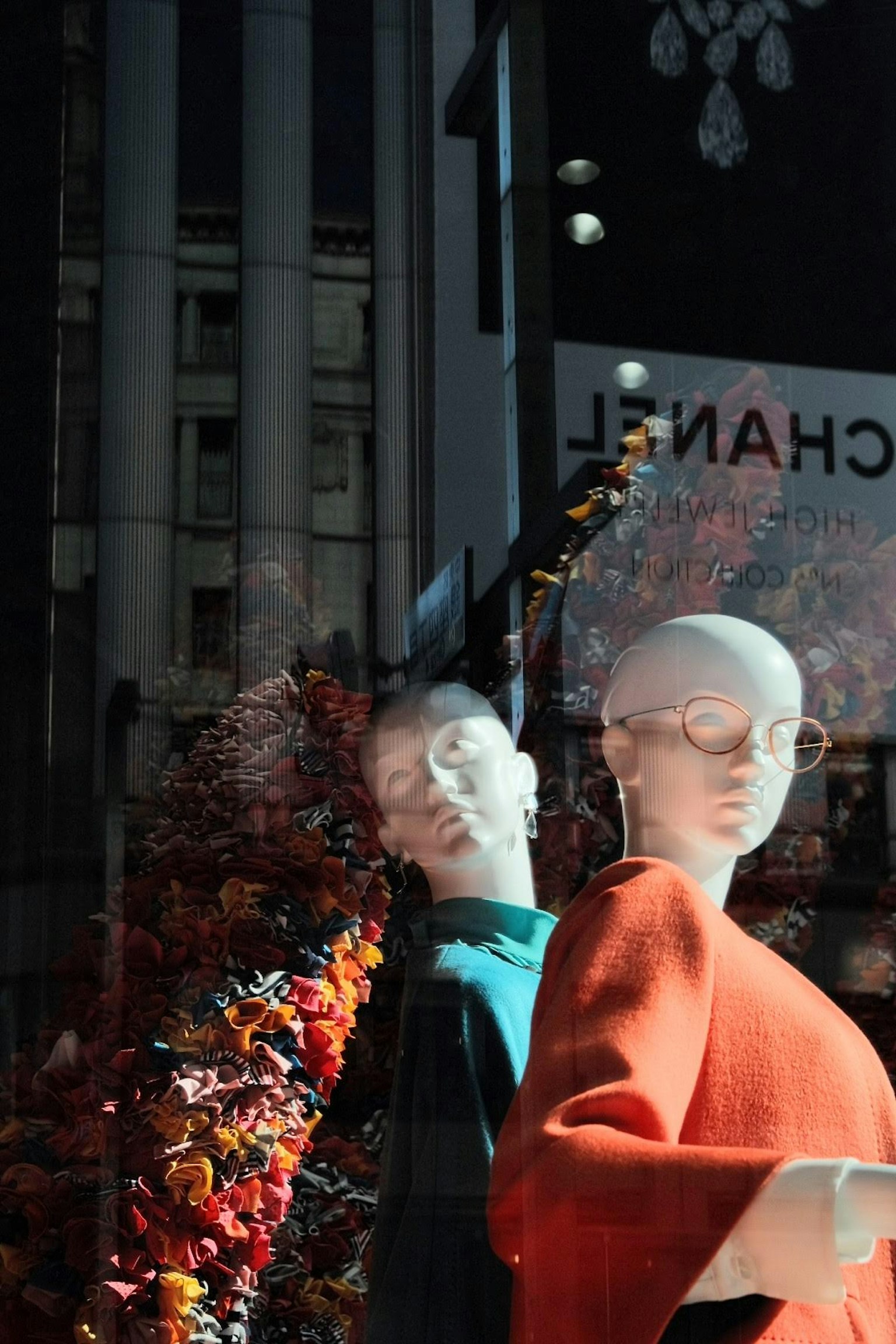 Mannequins in a storefront wearing orange clothing with colorful flowers in the background