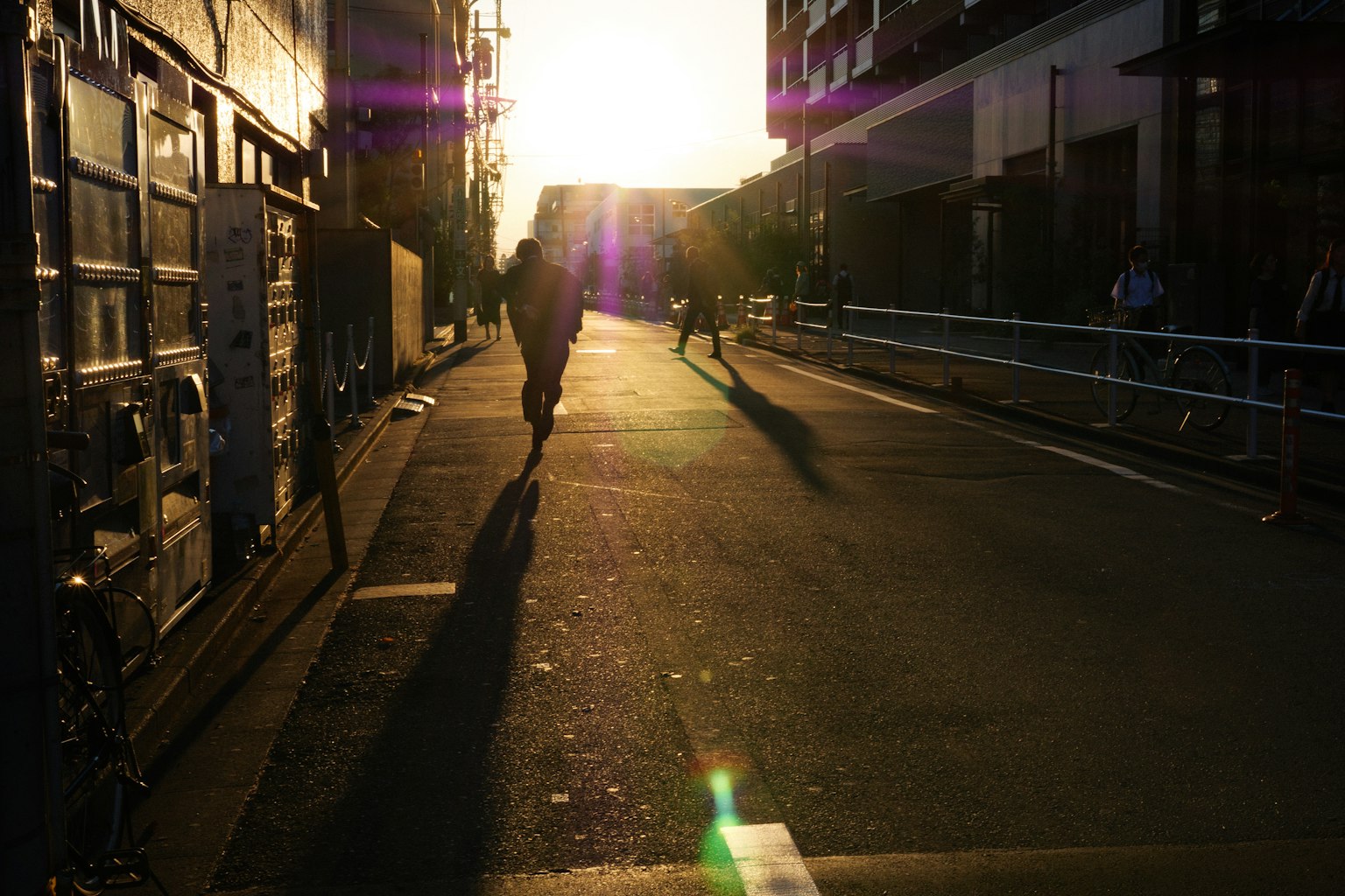 Silhouetten von Menschen, die bei Sonnenuntergang auf einer Straße mit langen Schatten gehen