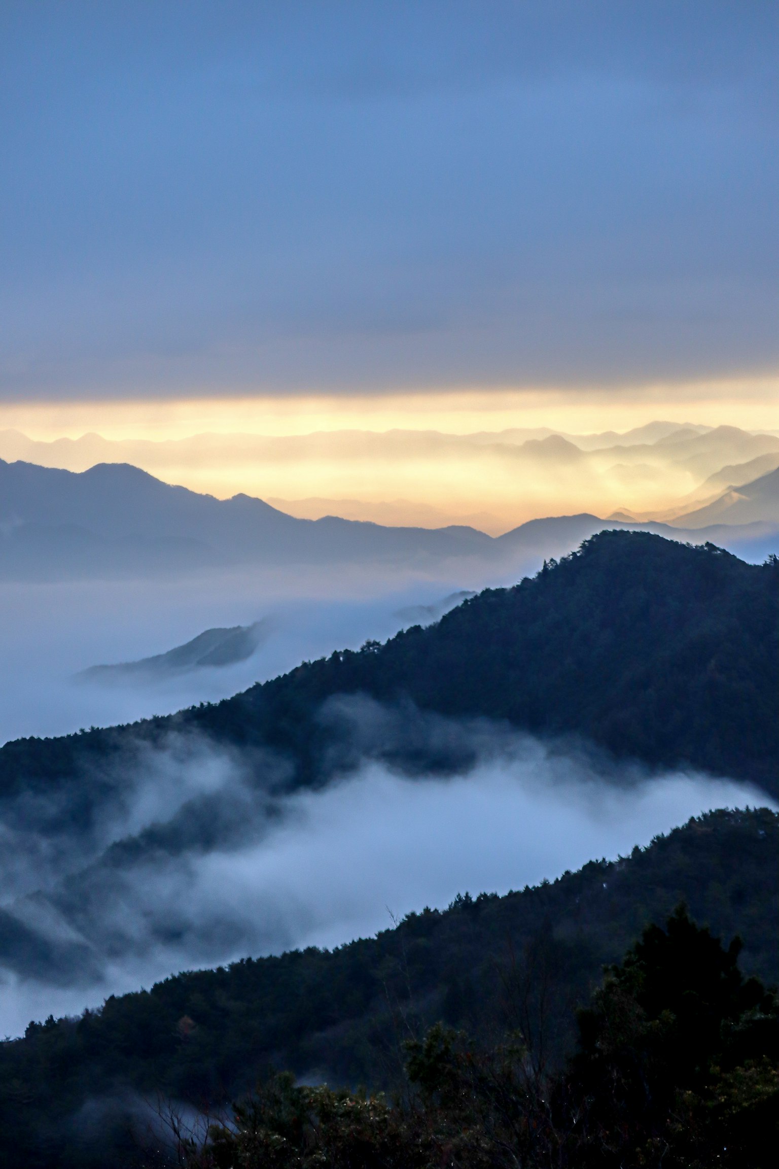 ภูเขาสีน้ำเงินที่ถูกหมอกปกคลุมกับท้องฟ้าสีส้มในตอนรุ่งเช้า