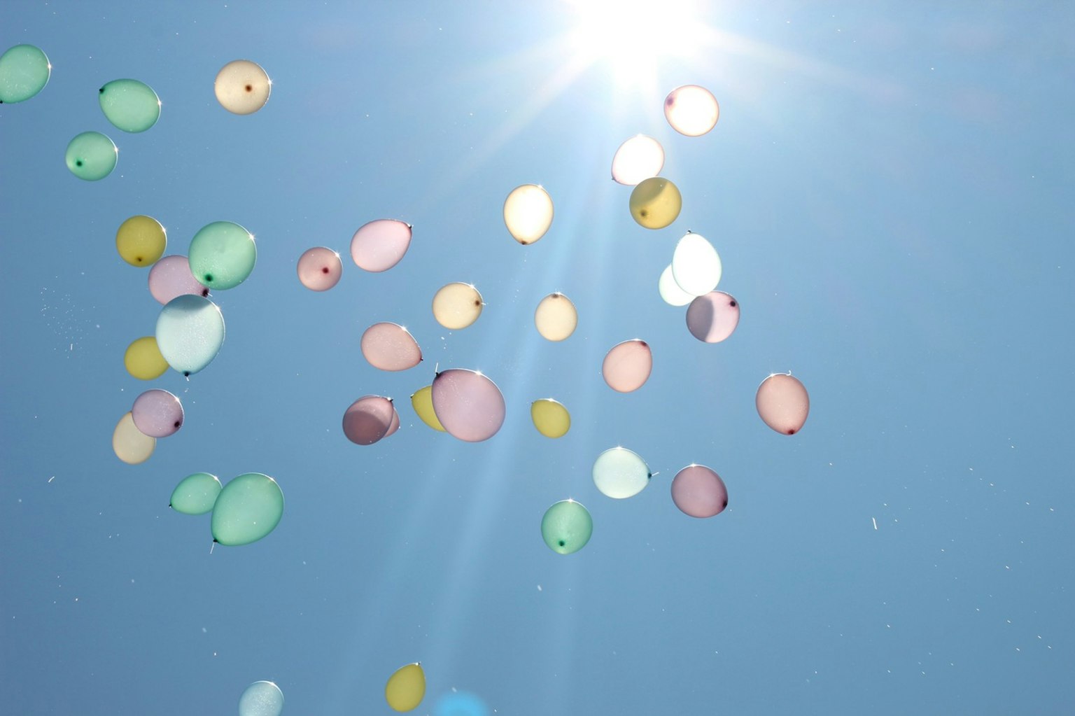 Balon berwarna-warni mengapung di langit biru yang diterangi sinar matahari