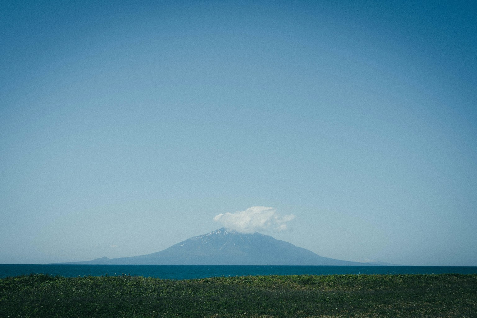 Pulau vulkan dengan awan di atas dan langit biru