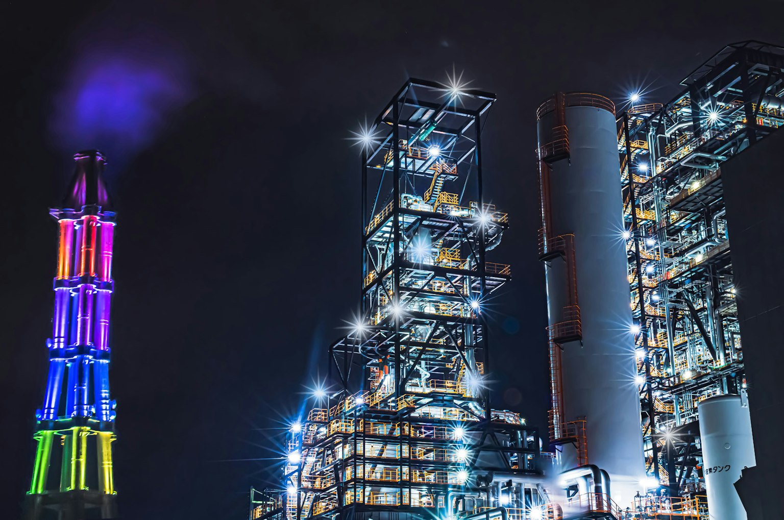 Beleuchtetes Industriegebäude bei Nacht mit buntem Schornstein und Strukturen