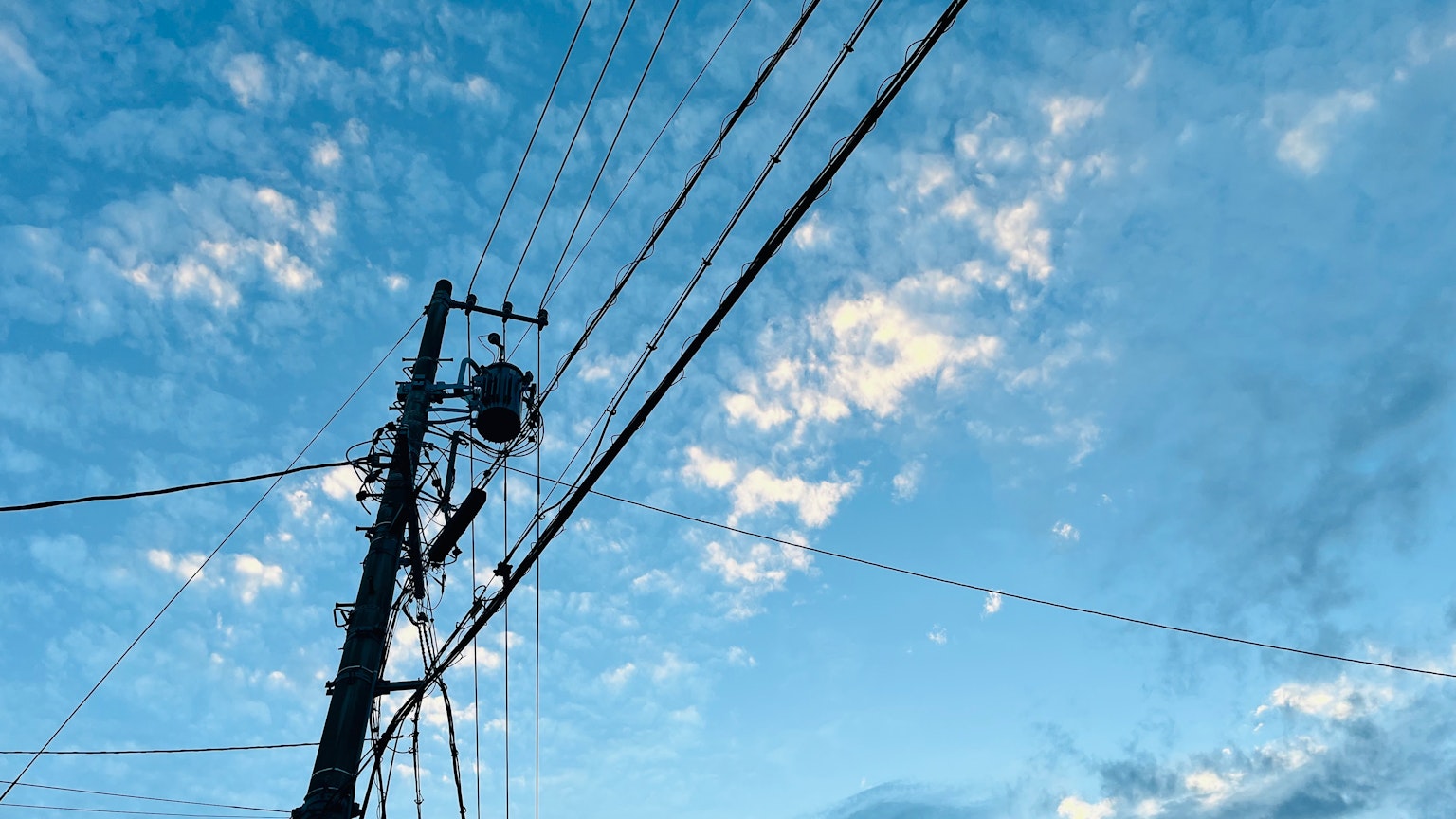 Poteau électrique et fils contre un ciel bleu avec des nuages blancs